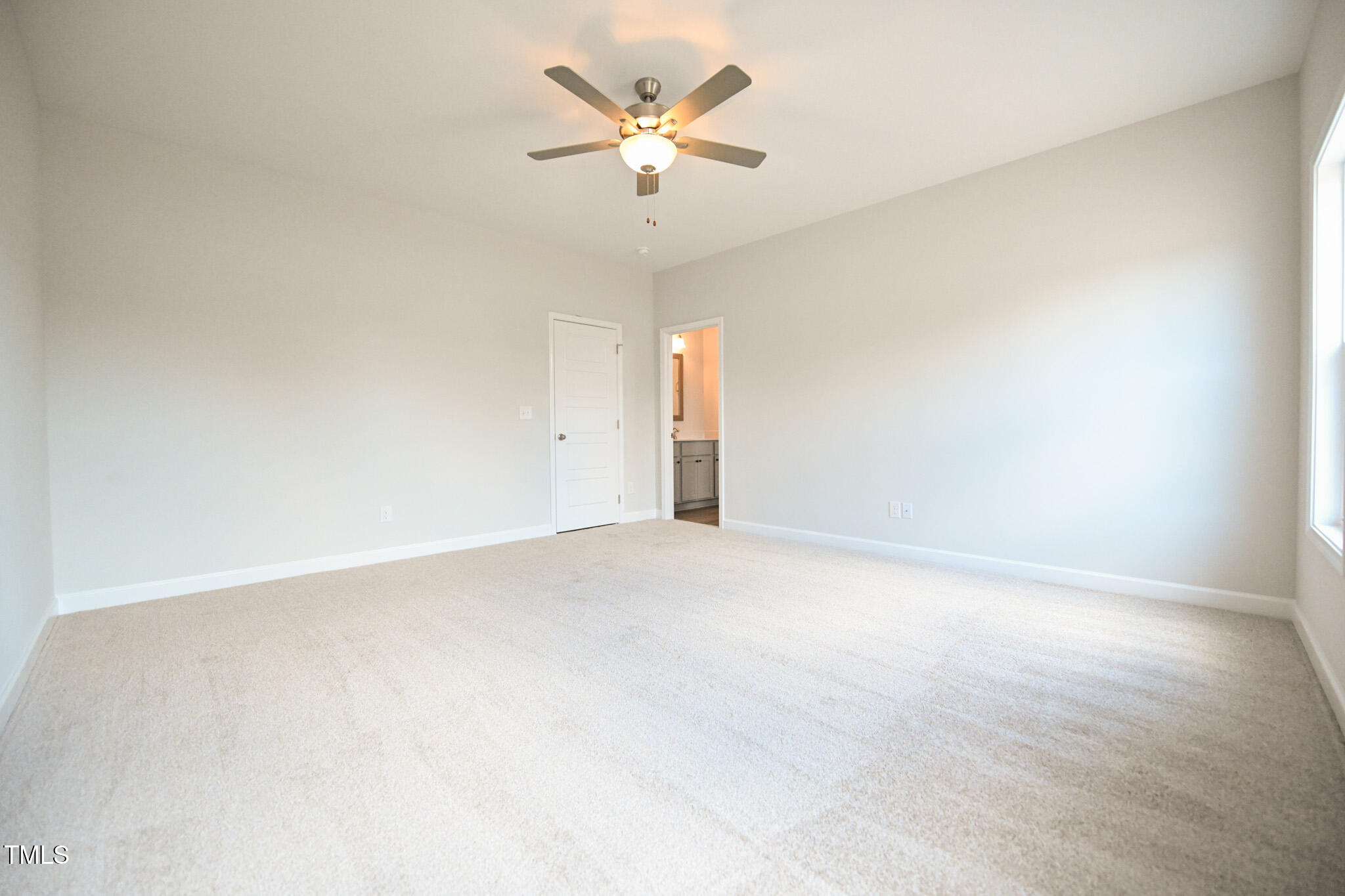 Empty carpeted bedroom with a ceiling fan and an open doorway to the bathroom.