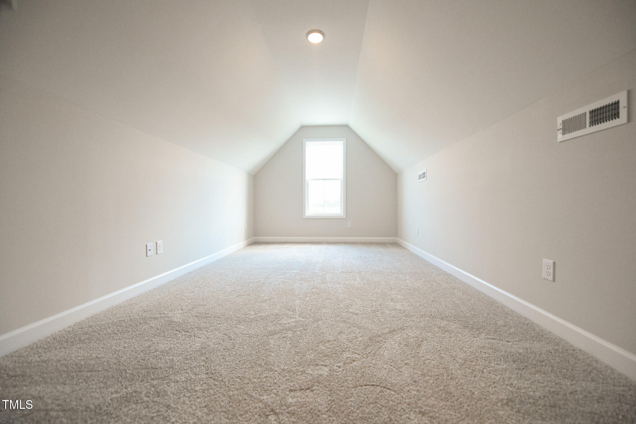 Empty upstairs room with beige carpet, sloped ceiling, and a window at the far end.