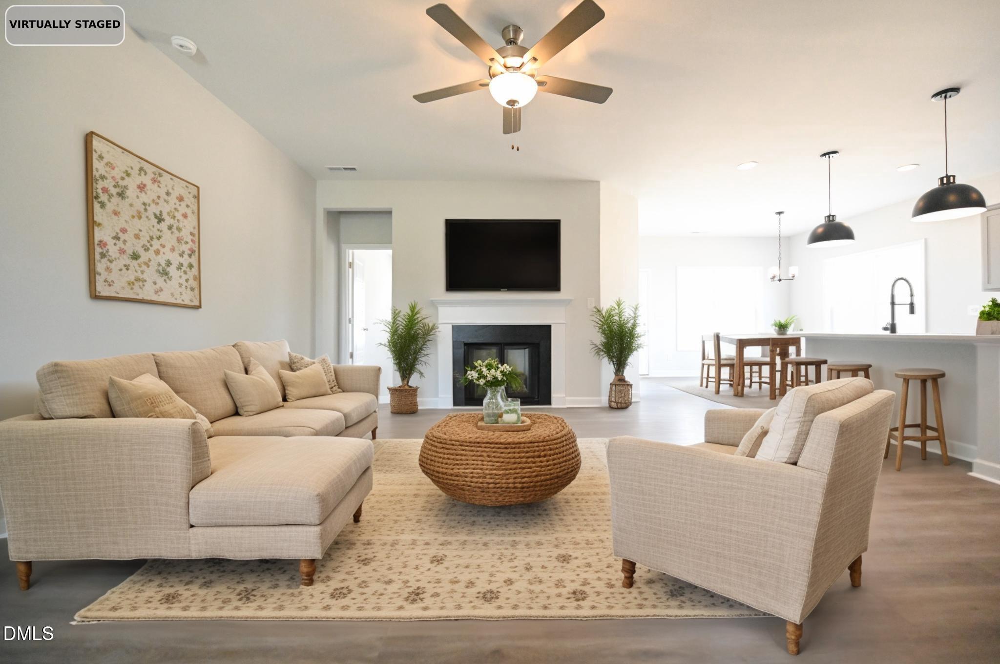 Virtually staged living room with a beige sectional, woven coffee table, fireplace, and open kitchen.