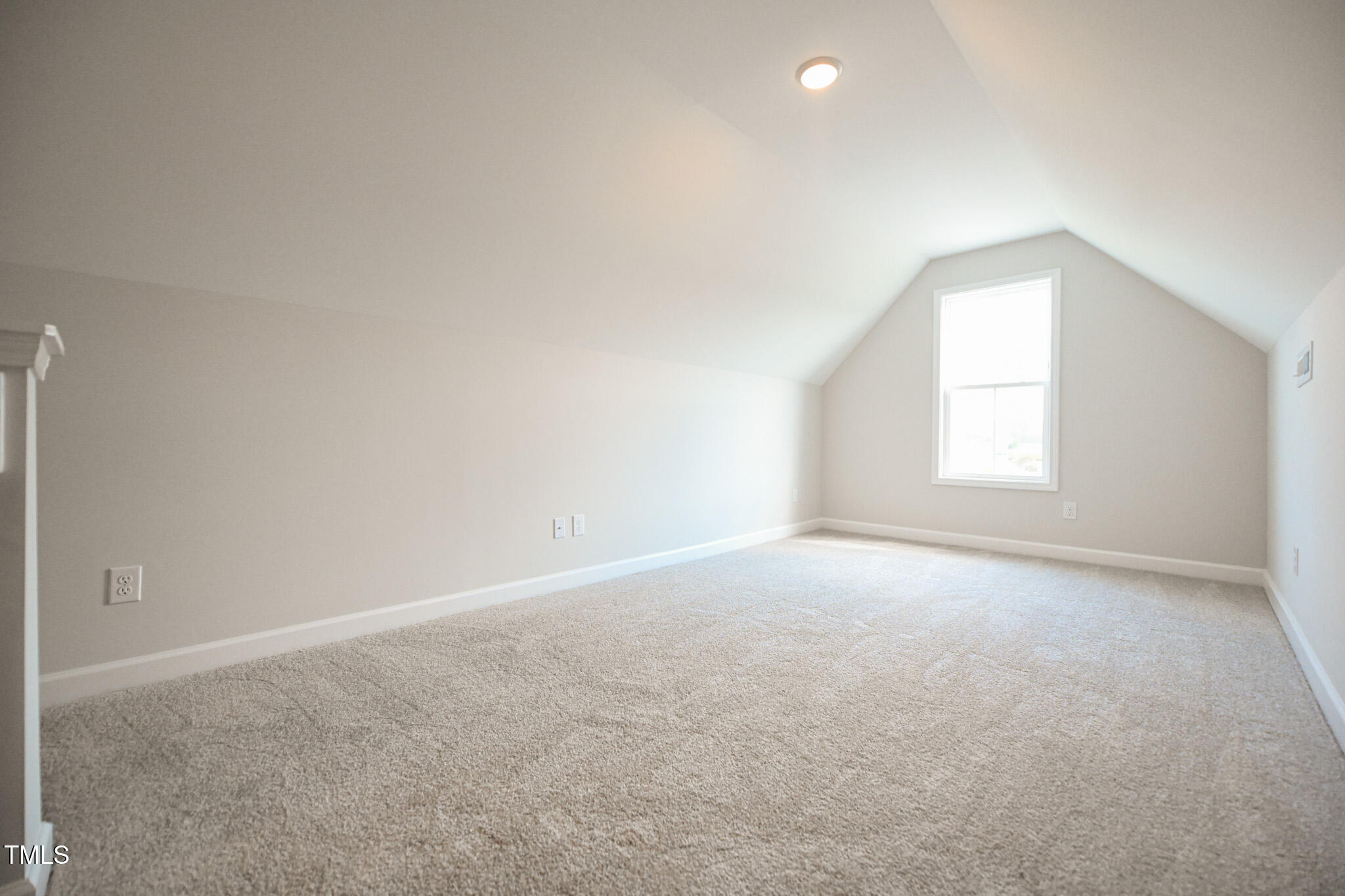 Vacant carpeted room with a sloped ceiling and a single window.