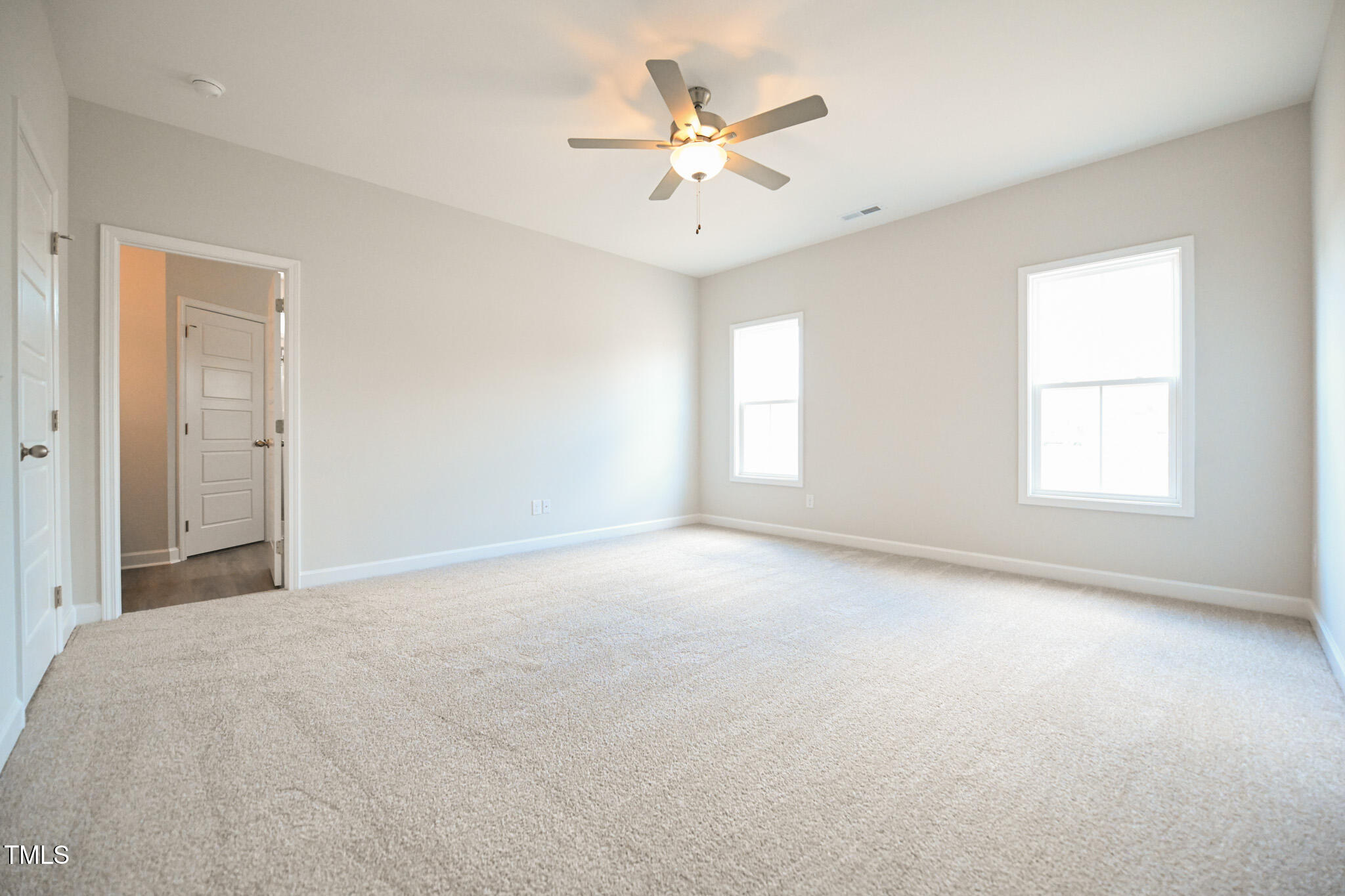 Empty carpeted bedroom with two windows and a lit ceiling fan.