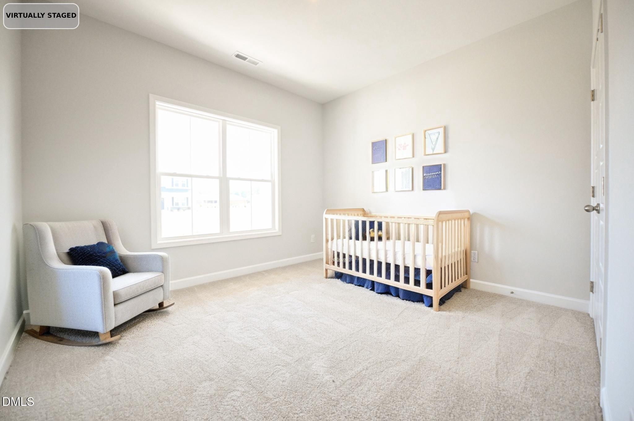 Virtually staged nursery with a light wood crib, navy bedding, and gray rocking chair.