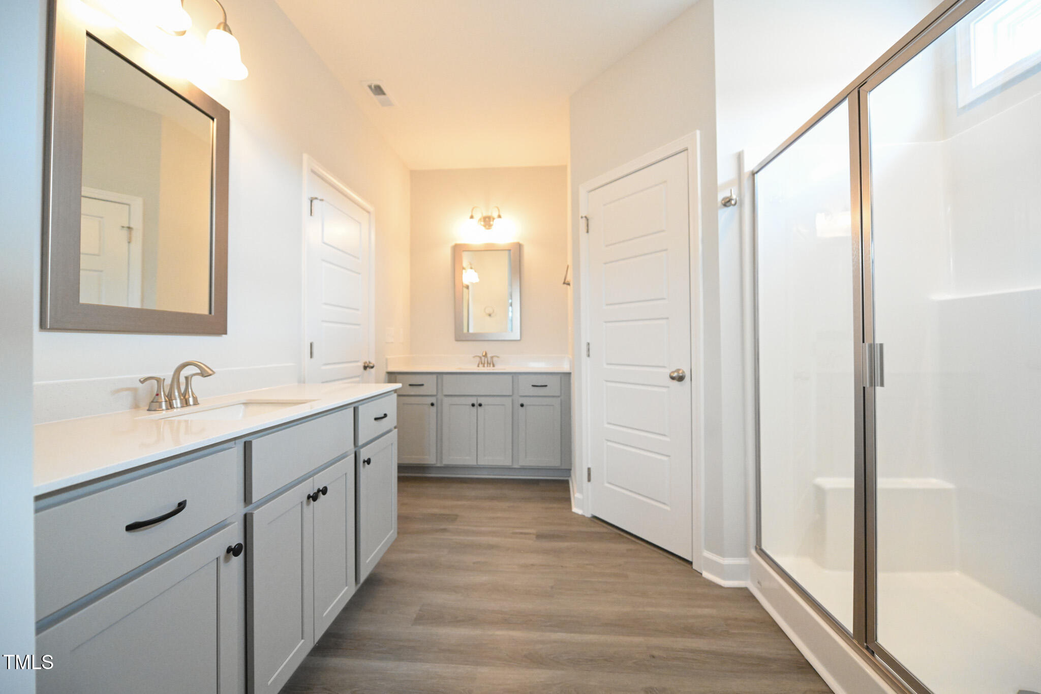 Bathroom with a long double vanity, gray cabinetry, framed mirrors, and a glass-enclosed shower.