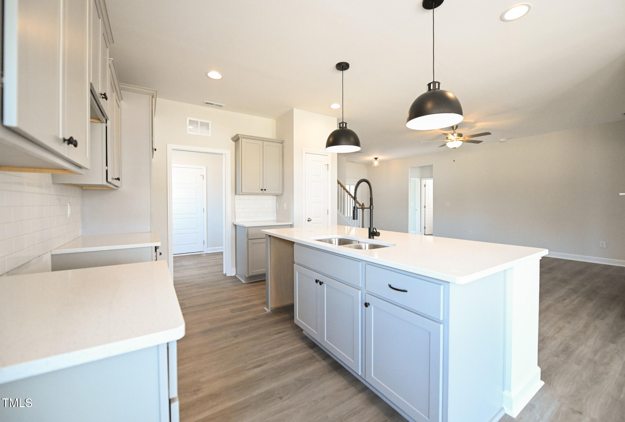 Kitchen with a large white island, double-basin sink, spring faucet, and black pendant lights.