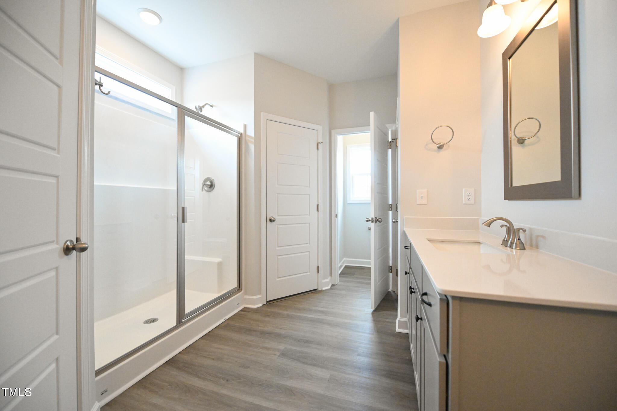 Bathroom with a glass walk-in shower, white vanity, framed mirror, and gray plank flooring.