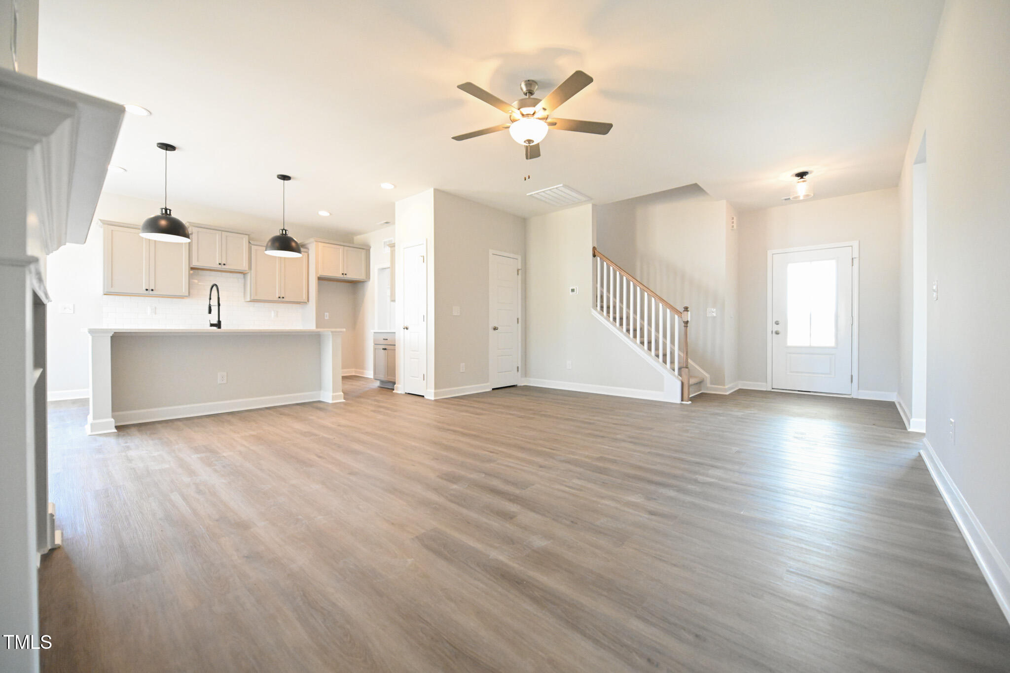 Open living room with gray wood-look floors, kitchen breakfast bar, and staircase.