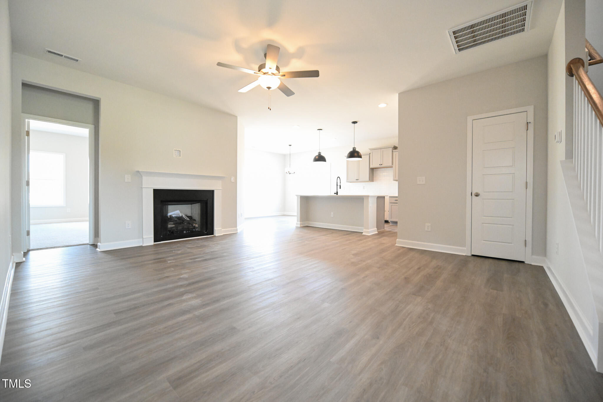 Vacant living room with a fireplace, gray wood-look floors, and an open kitchen with island.