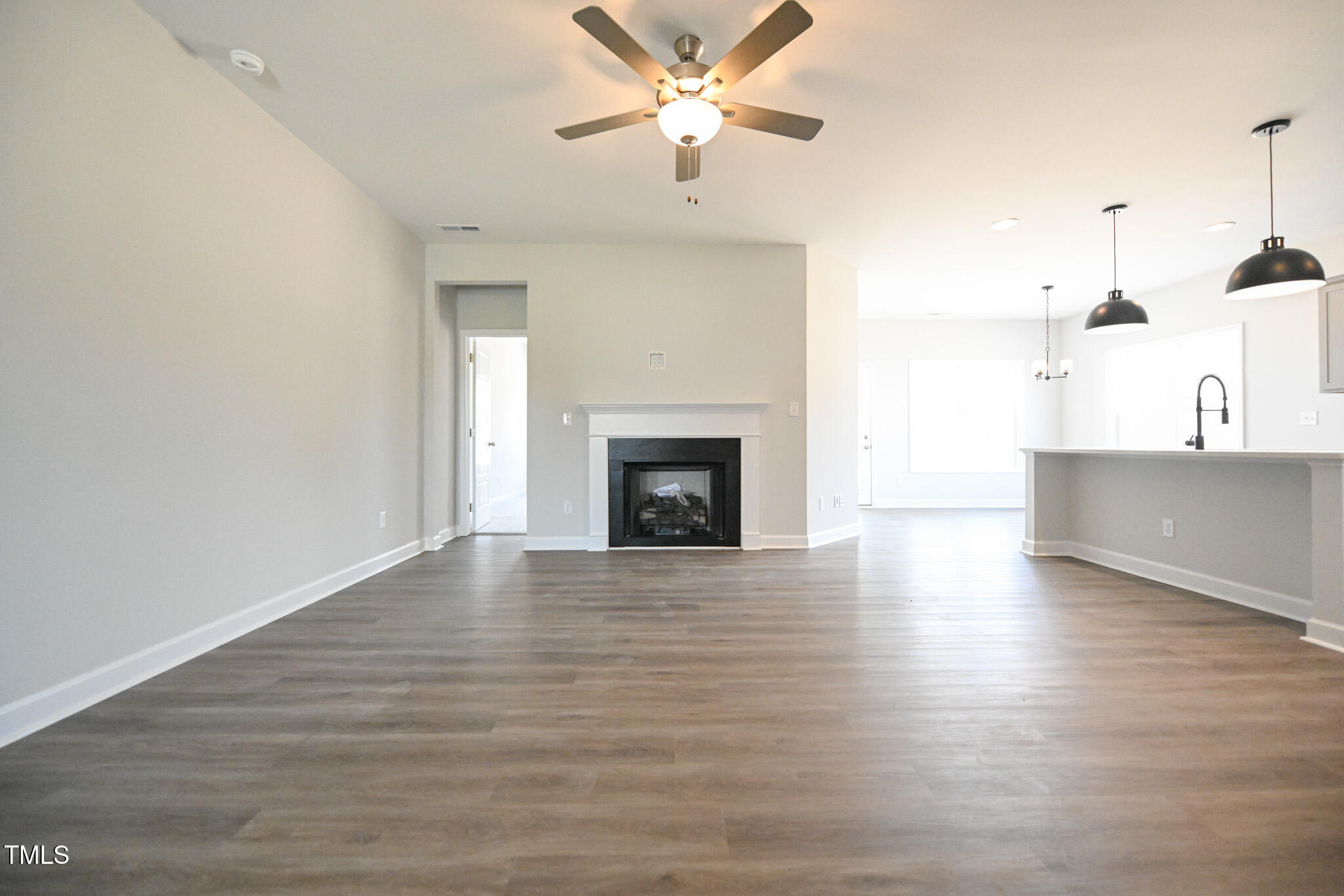 Unfurnished living room with a fireplace, gray wood-look floors, and an open kitchen with pendant lights.