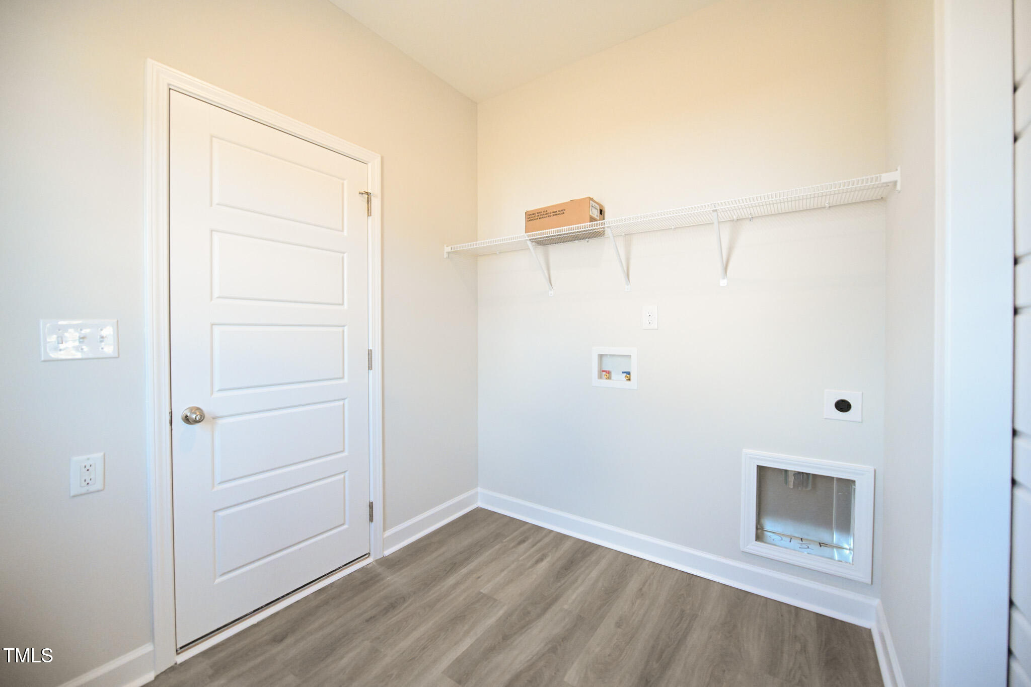 Vacant laundry room with a wire shelf, washer hookups, and a low pet door.