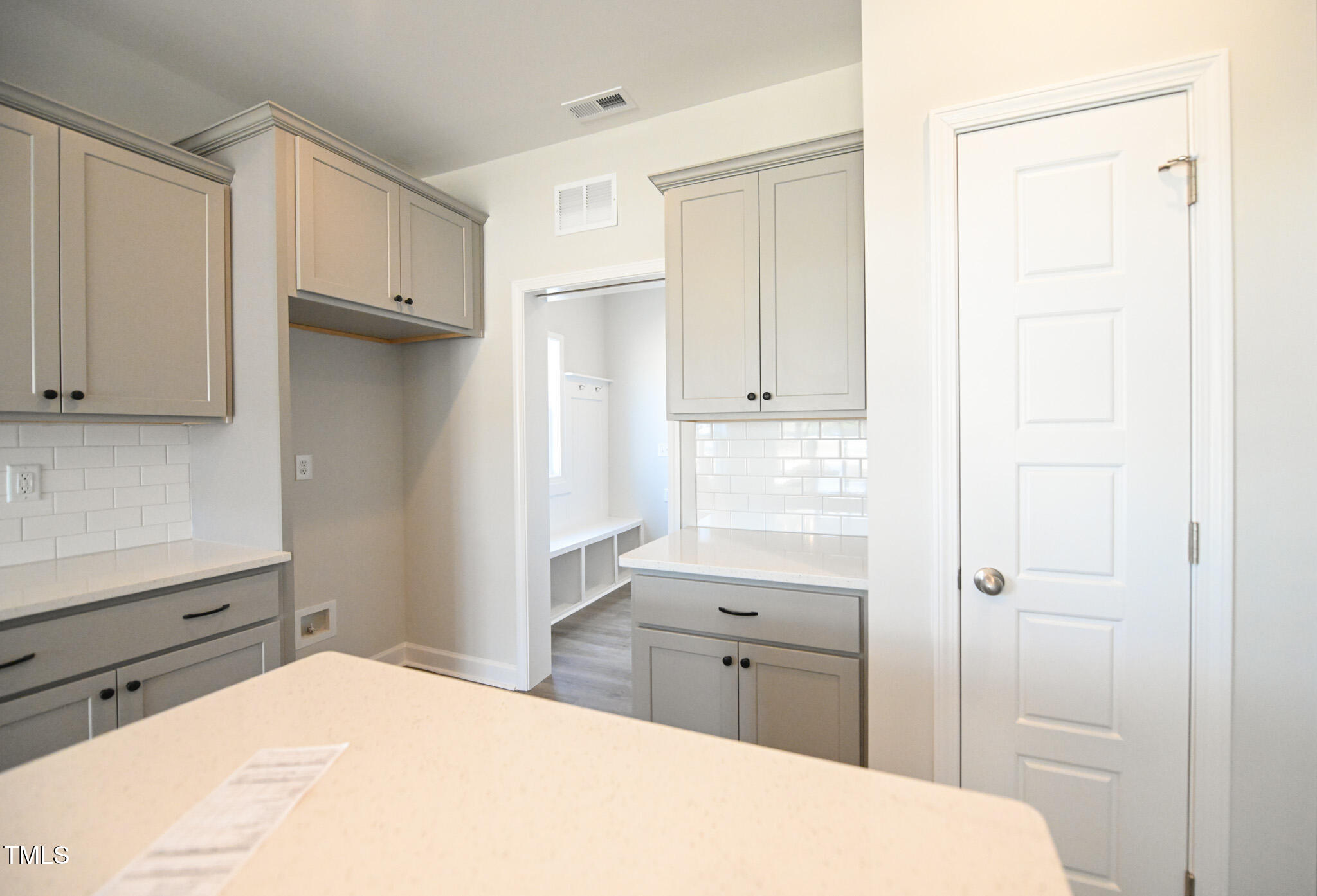 Kitchen with gray cabinets, white subway tile, and an adjoining built-in bench and cubbies.
