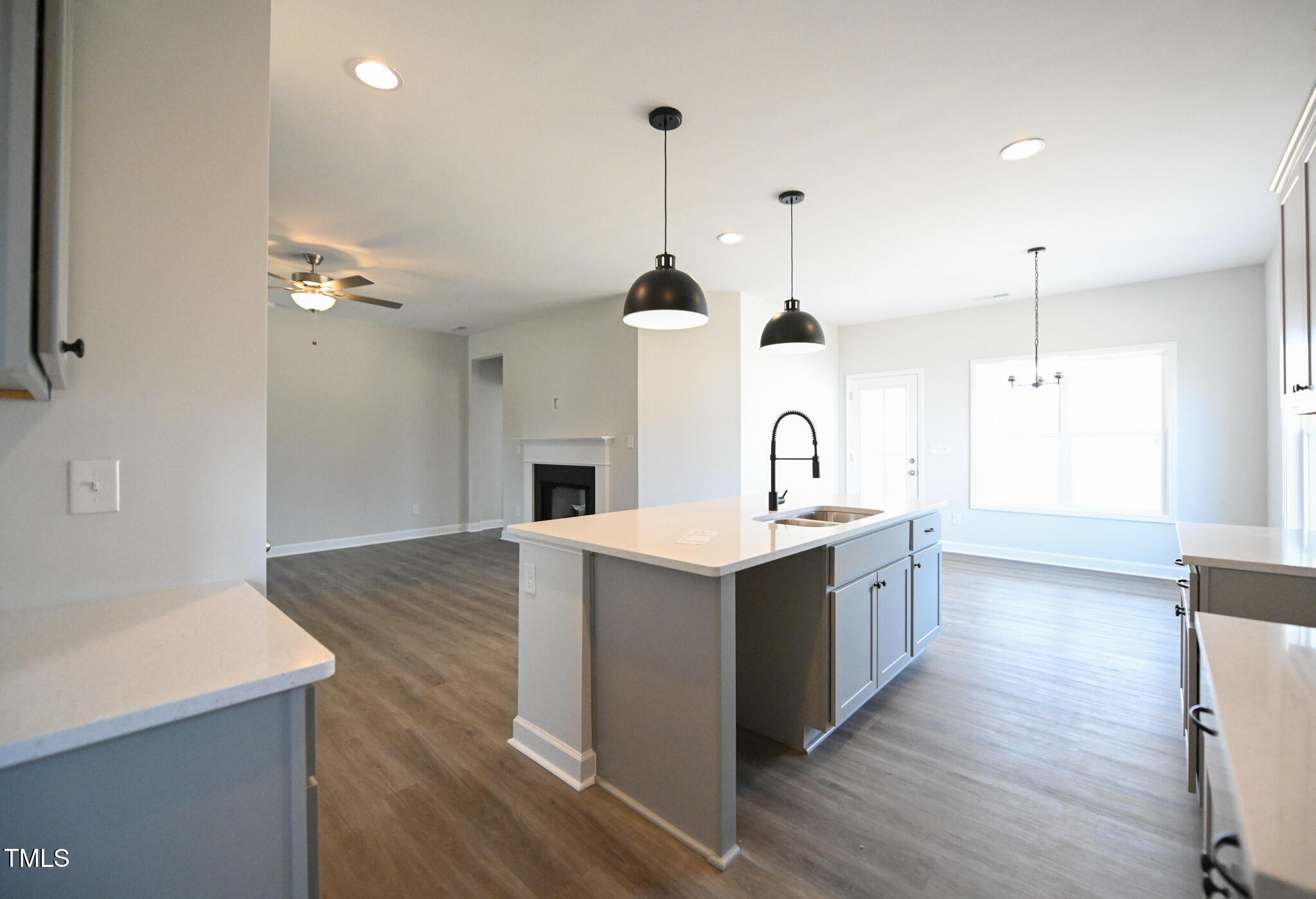 Open-plan kitchen with a large island, black pendant lights, and an adjoining living area with a fireplace.