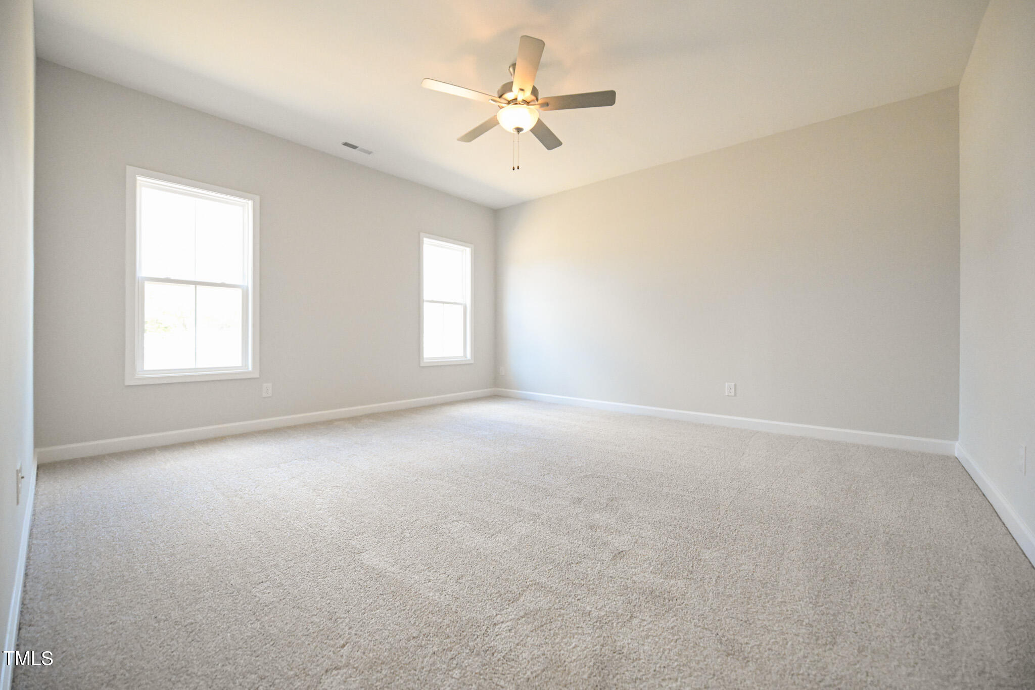 Empty bedroom with beige carpet, two windows, and a ceiling fan.