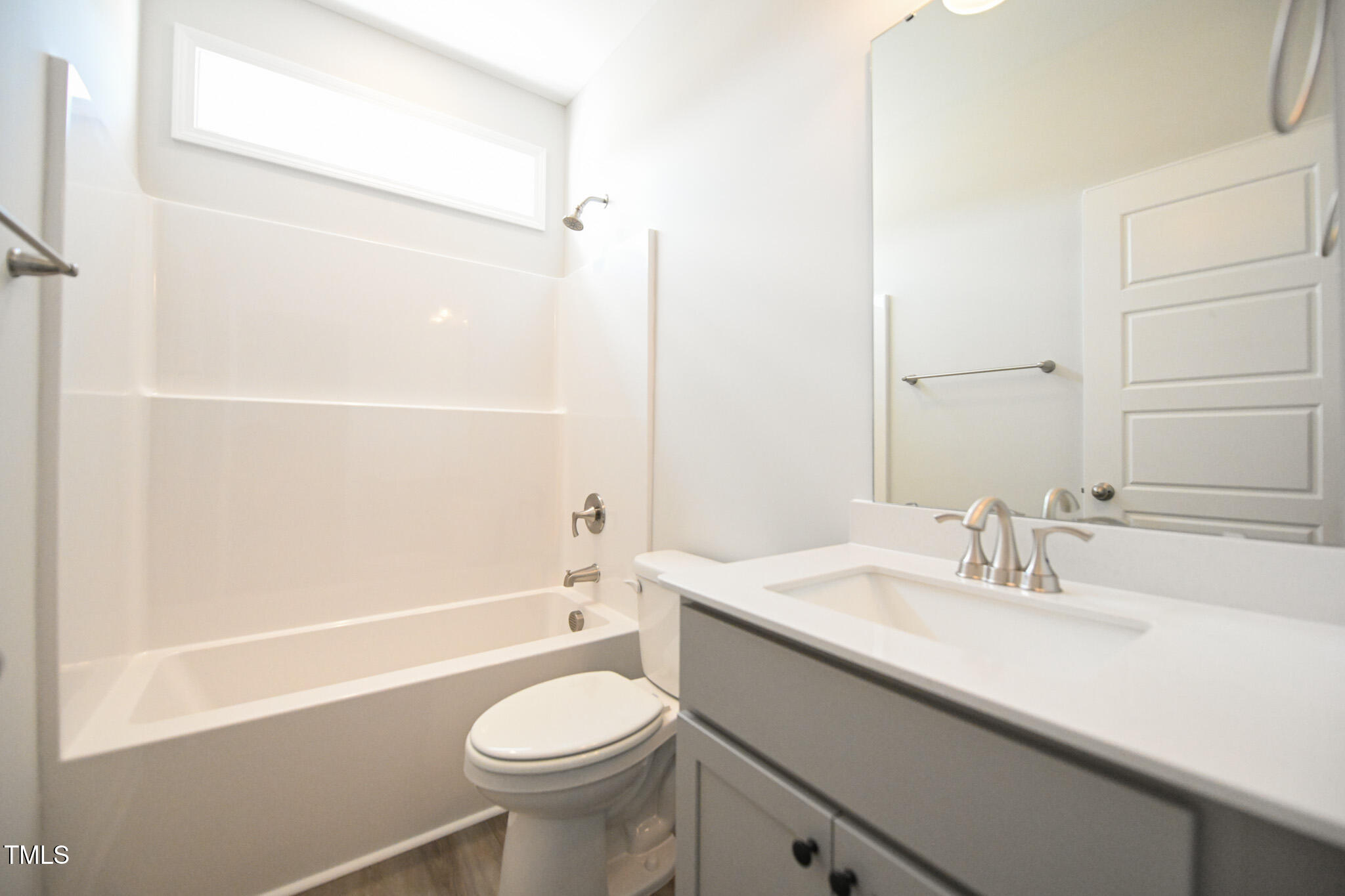 Bathroom with a tub and shower, toilet, and gray vanity beneath a large mirror.