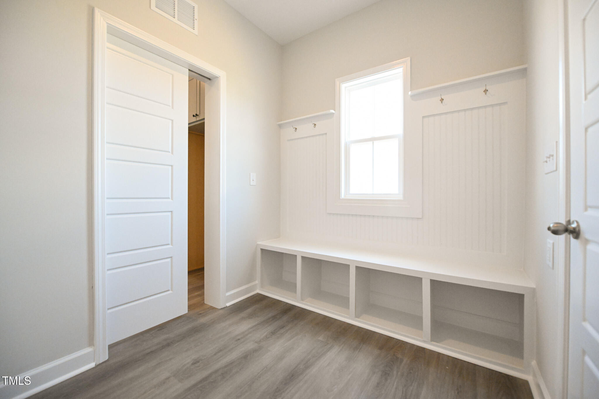 Mudroom with built-in bench, open cubbies, coat hooks, and a window.