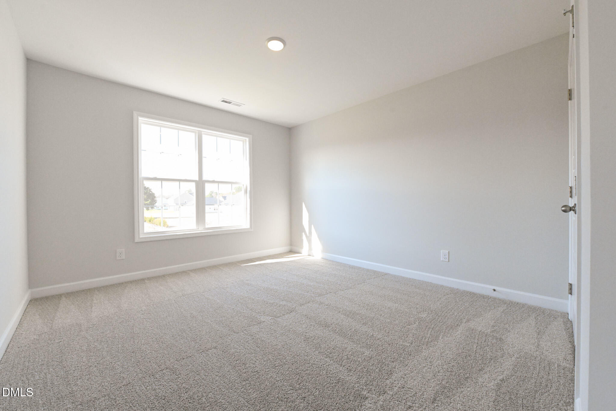 Vacant bedroom with beige carpet, gray walls, and a large sunlit window.