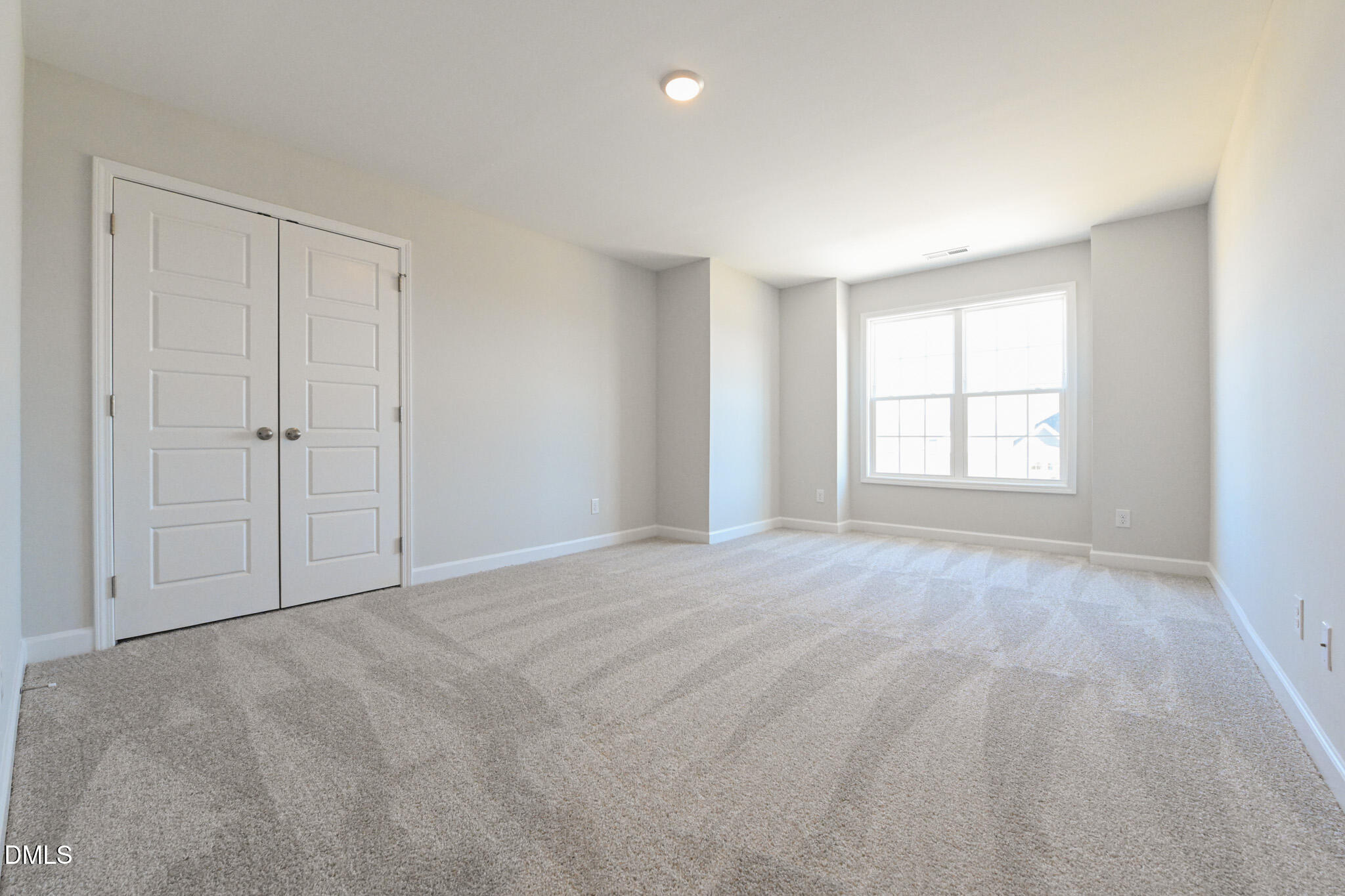 Empty carpeted bedroom with double closet doors and a large window.