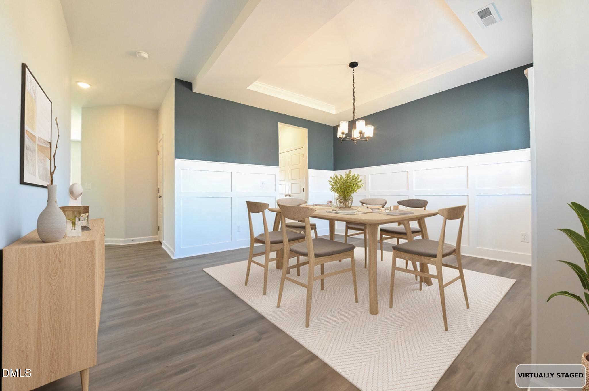 Dining room with a wood table and chairs, white paneled wainscoting, and a tray ceiling.