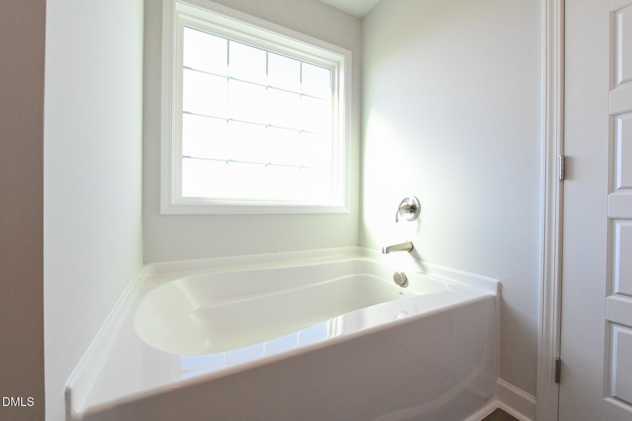 Built-in white bathtub beneath a large window, with chrome fixtures.