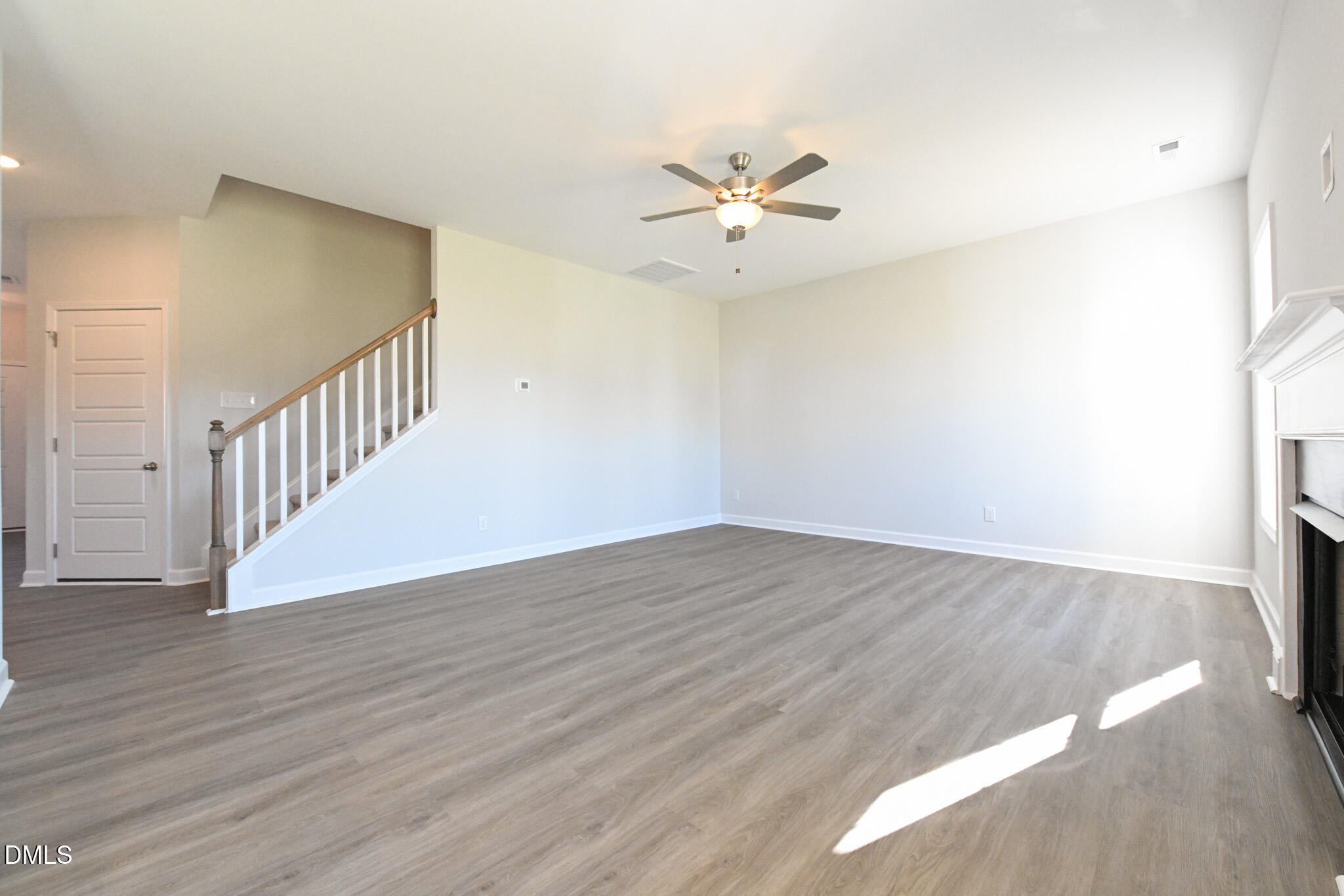 Vacant living room with a staircase, gray flooring, ceiling fan, and fireplace.