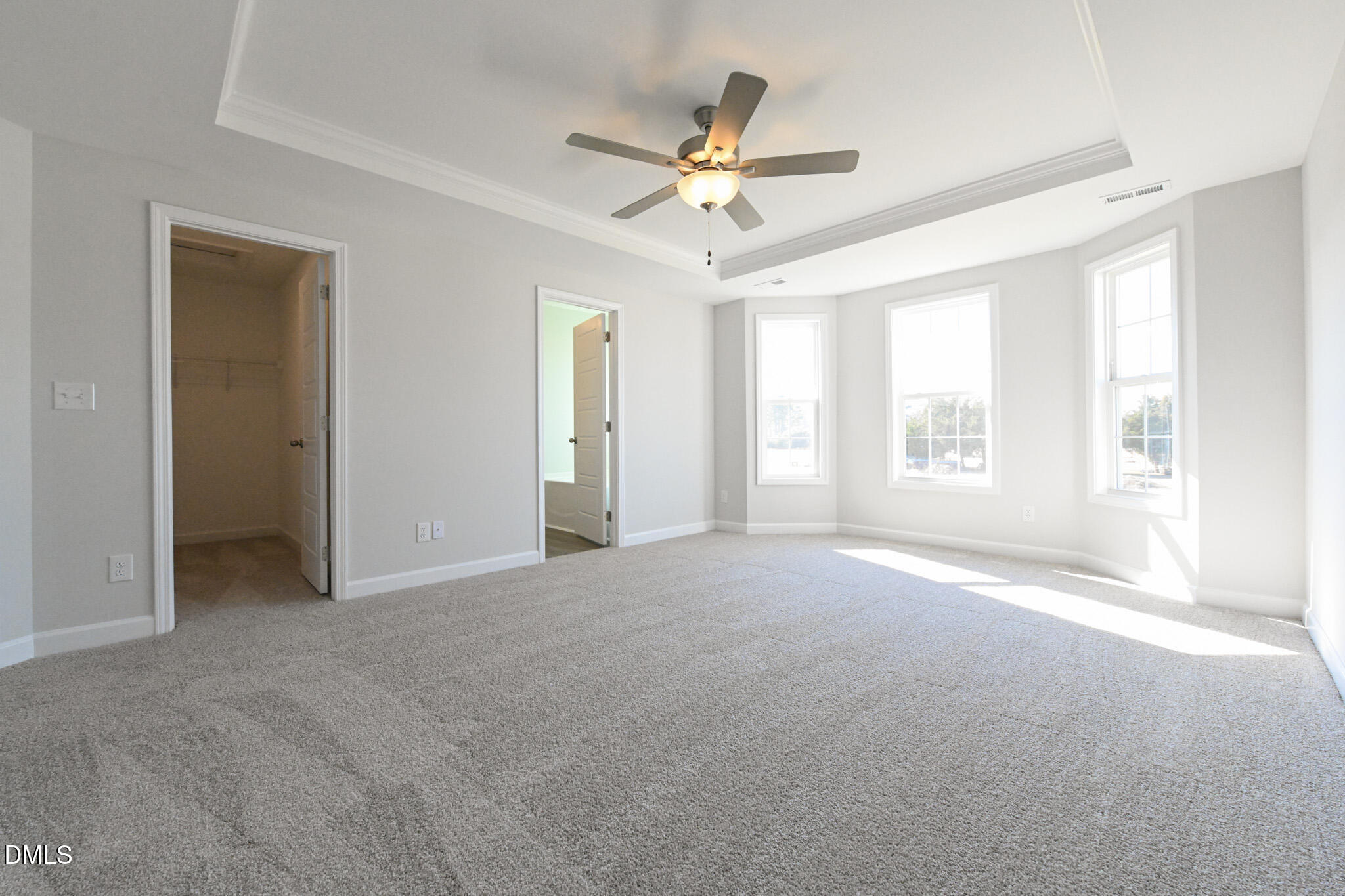 Empty carpeted bedroom with a tray ceiling, ceiling fan, and three bright windows.