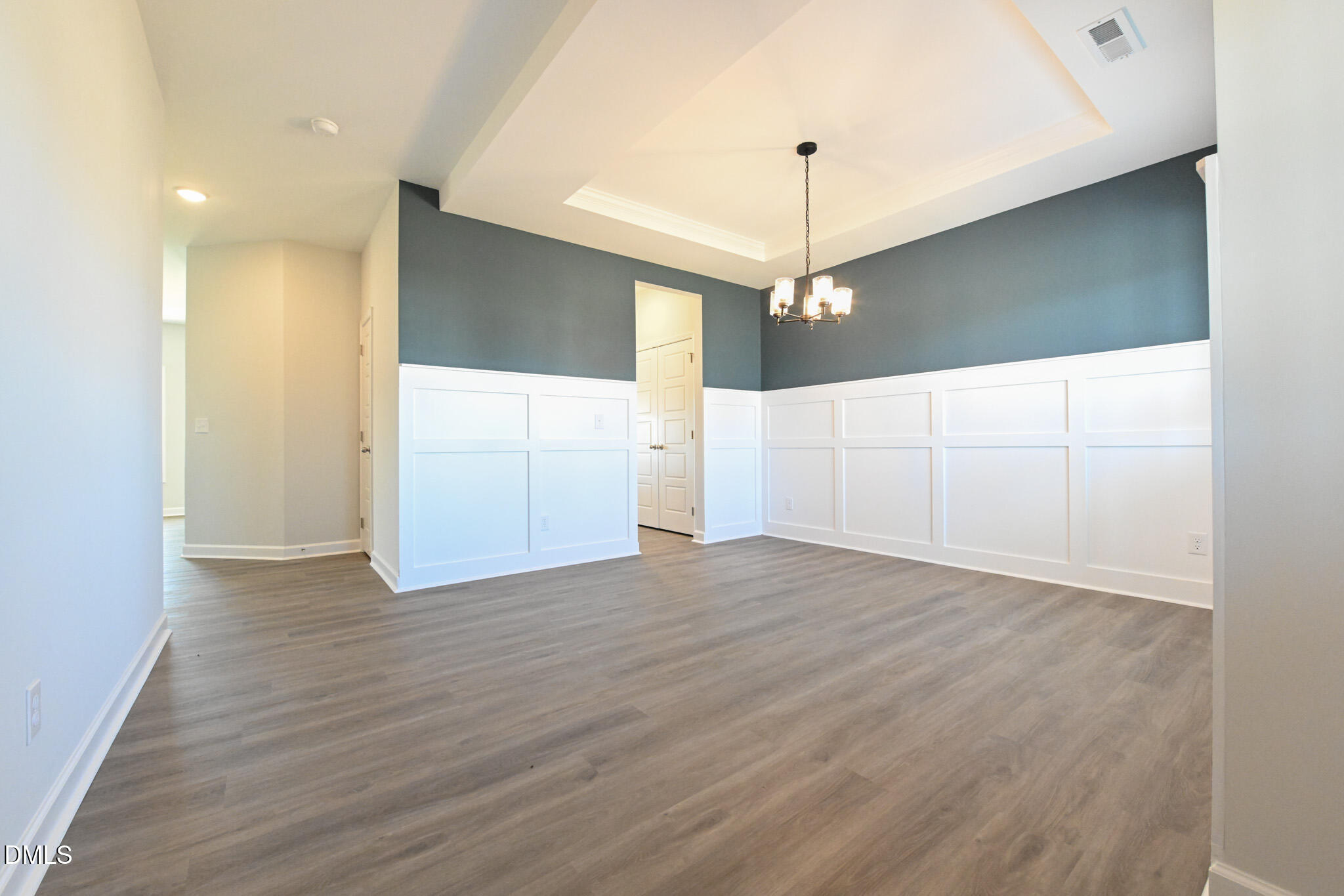 Empty dining room with white paneled wainscoting, gray flooring, and a tray ceiling.