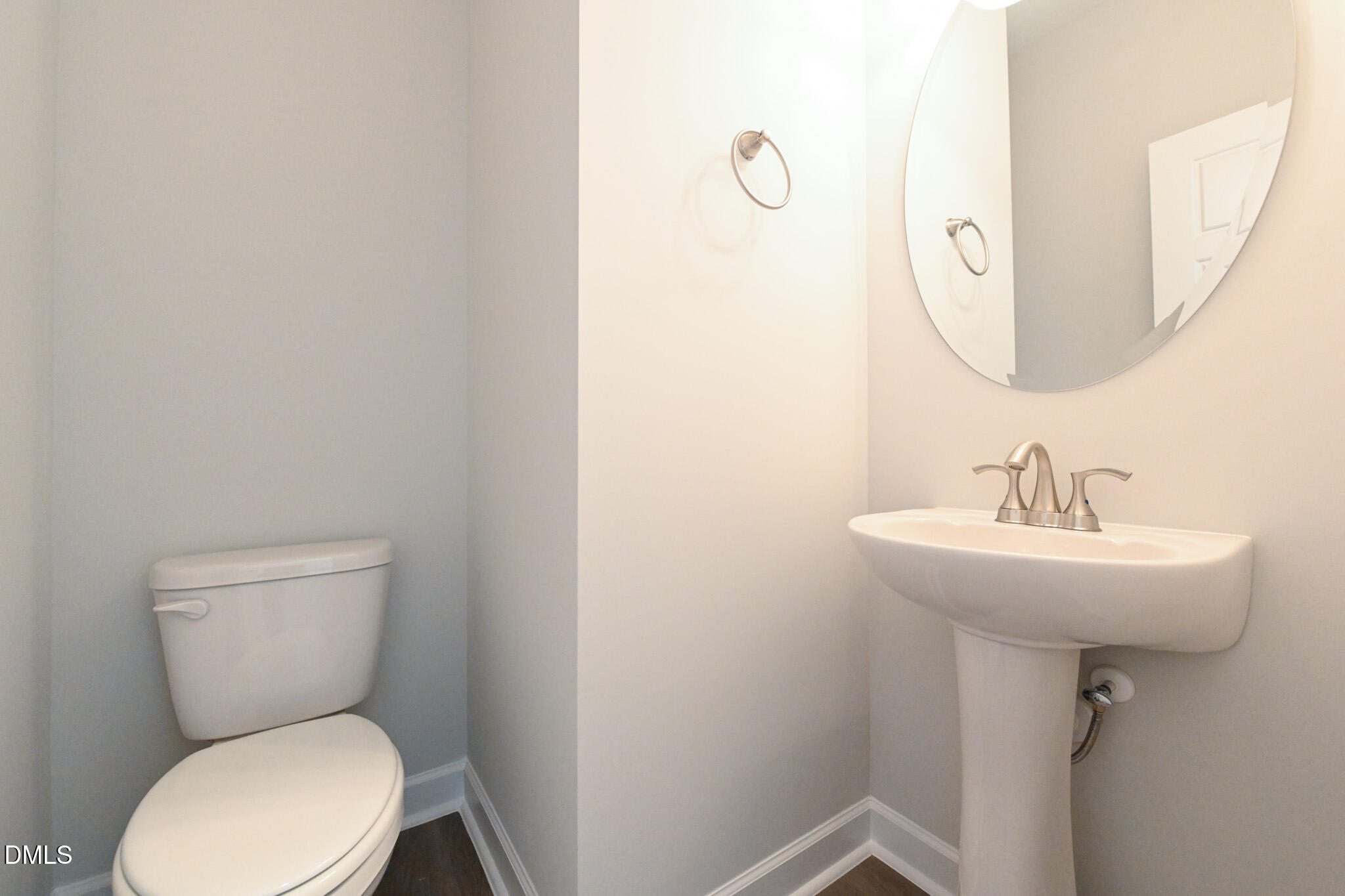 Half bathroom with a white toilet, pedestal sink, round mirror, and chrome fixtures.