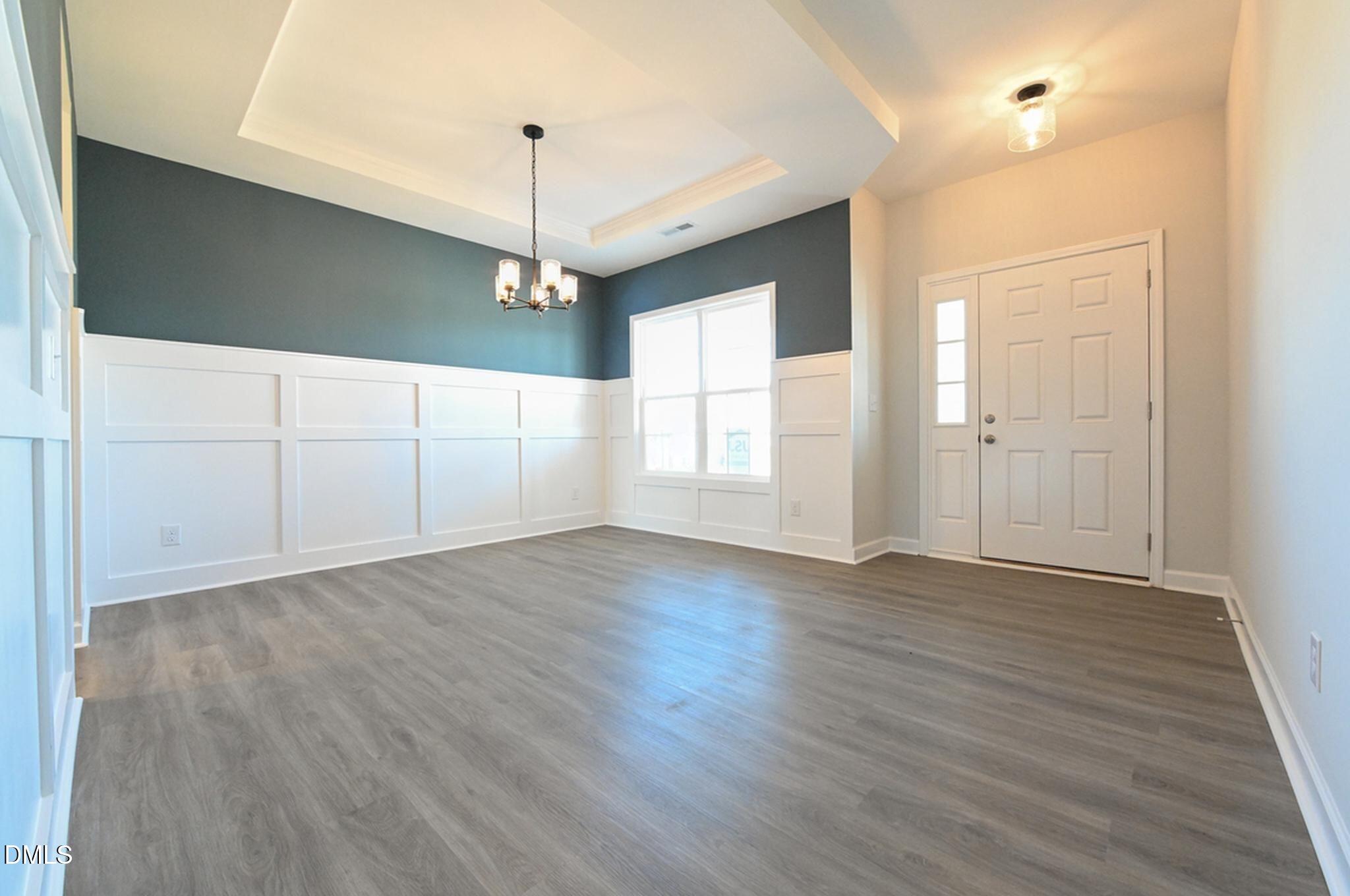 Vacant entry foyer with gray flooring, paneled walls, a teal accent wall, and a tray ceiling.