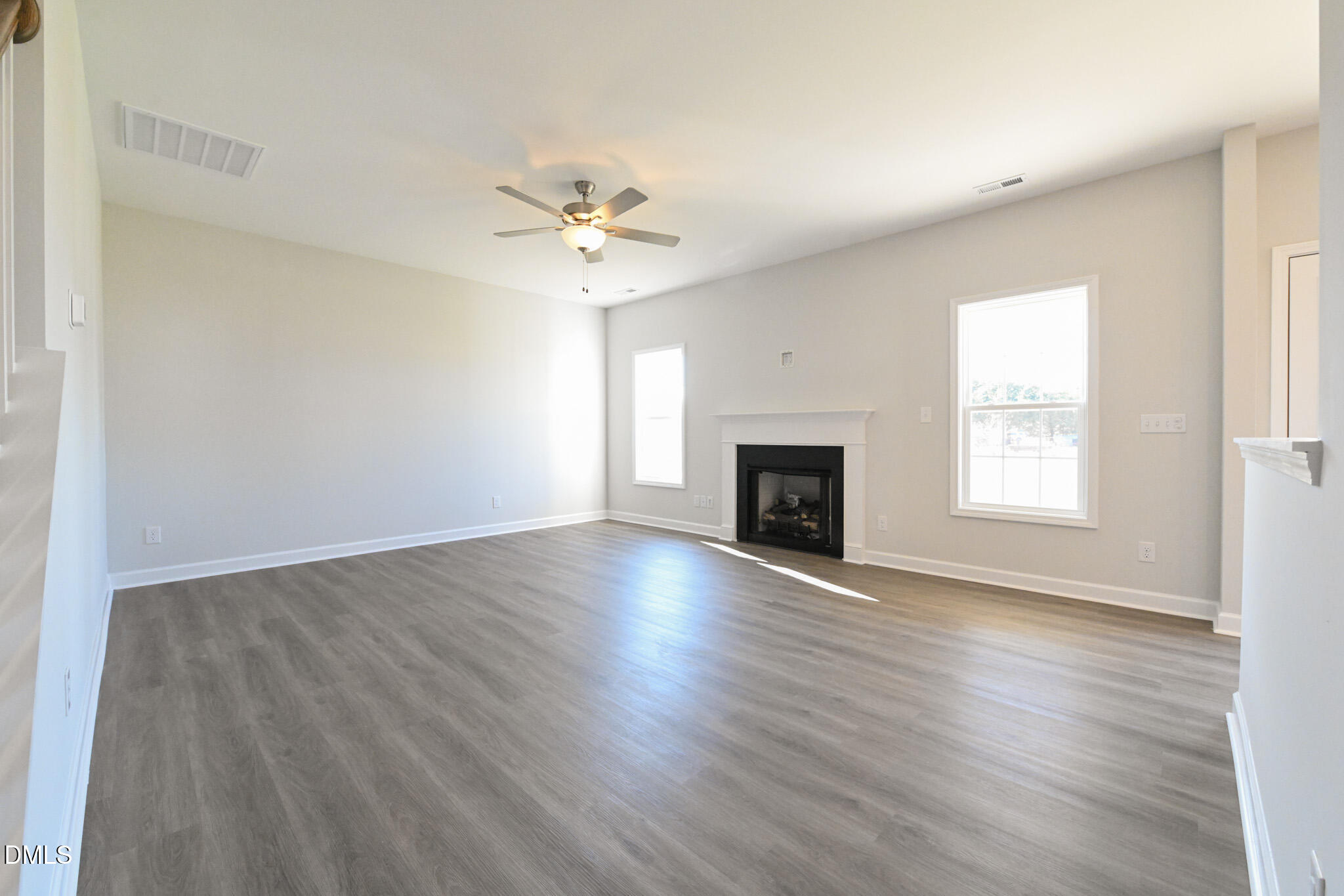 Empty living room with gray plank floors, a fireplace, ceiling fan, and two windows.