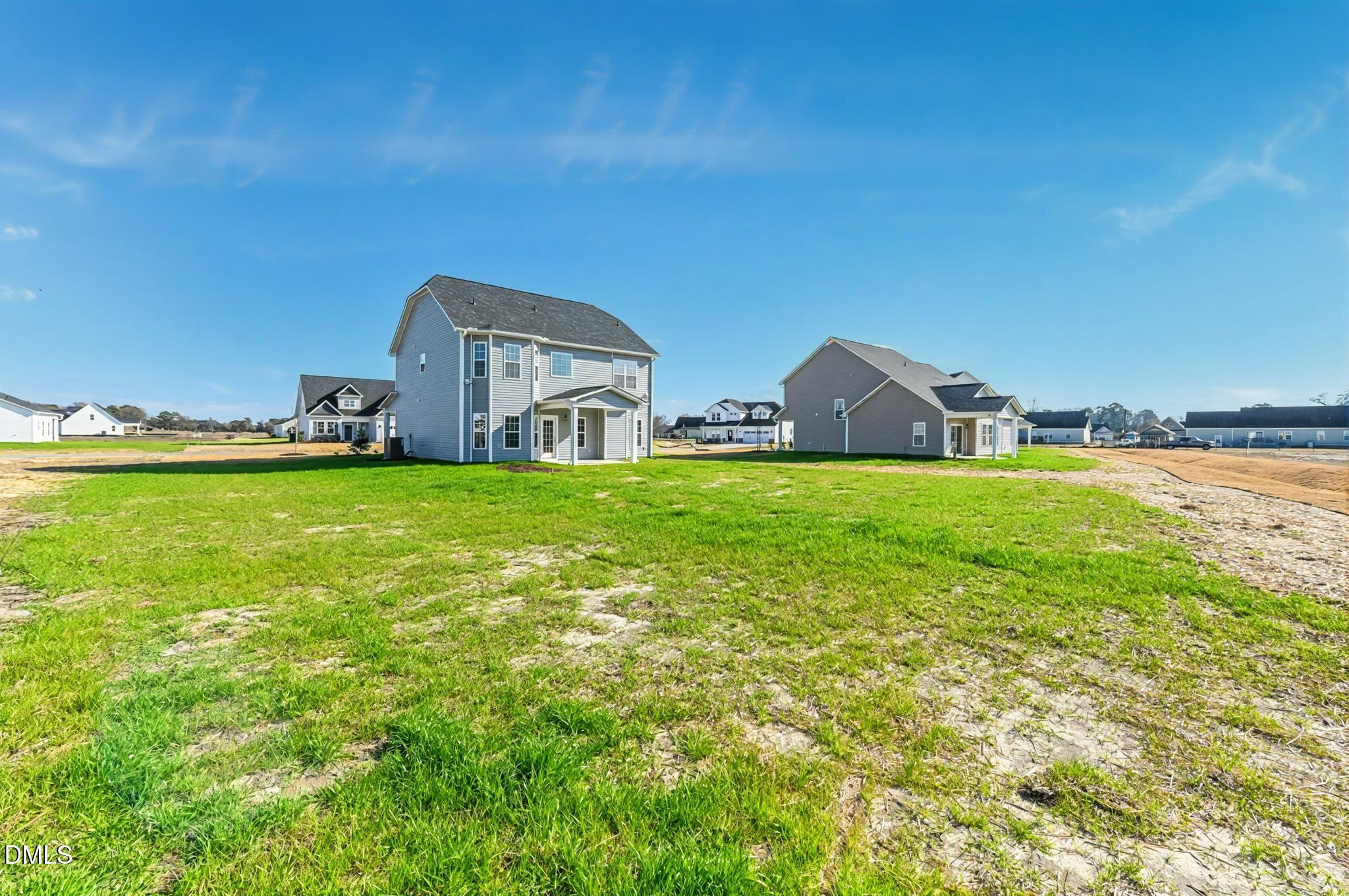 Gray two-story home and neighboring houses beyond a broad, partly bare grassy yard.