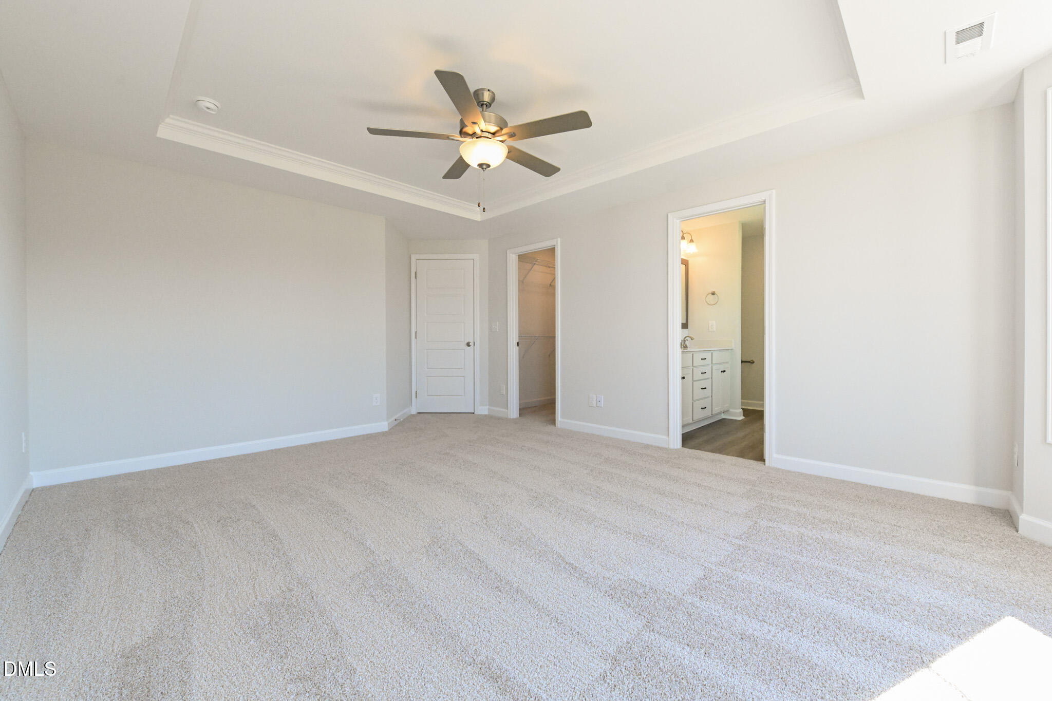 Empty carpeted bedroom with a tray ceiling, ceiling fan, closet, and adjoining bathroom.