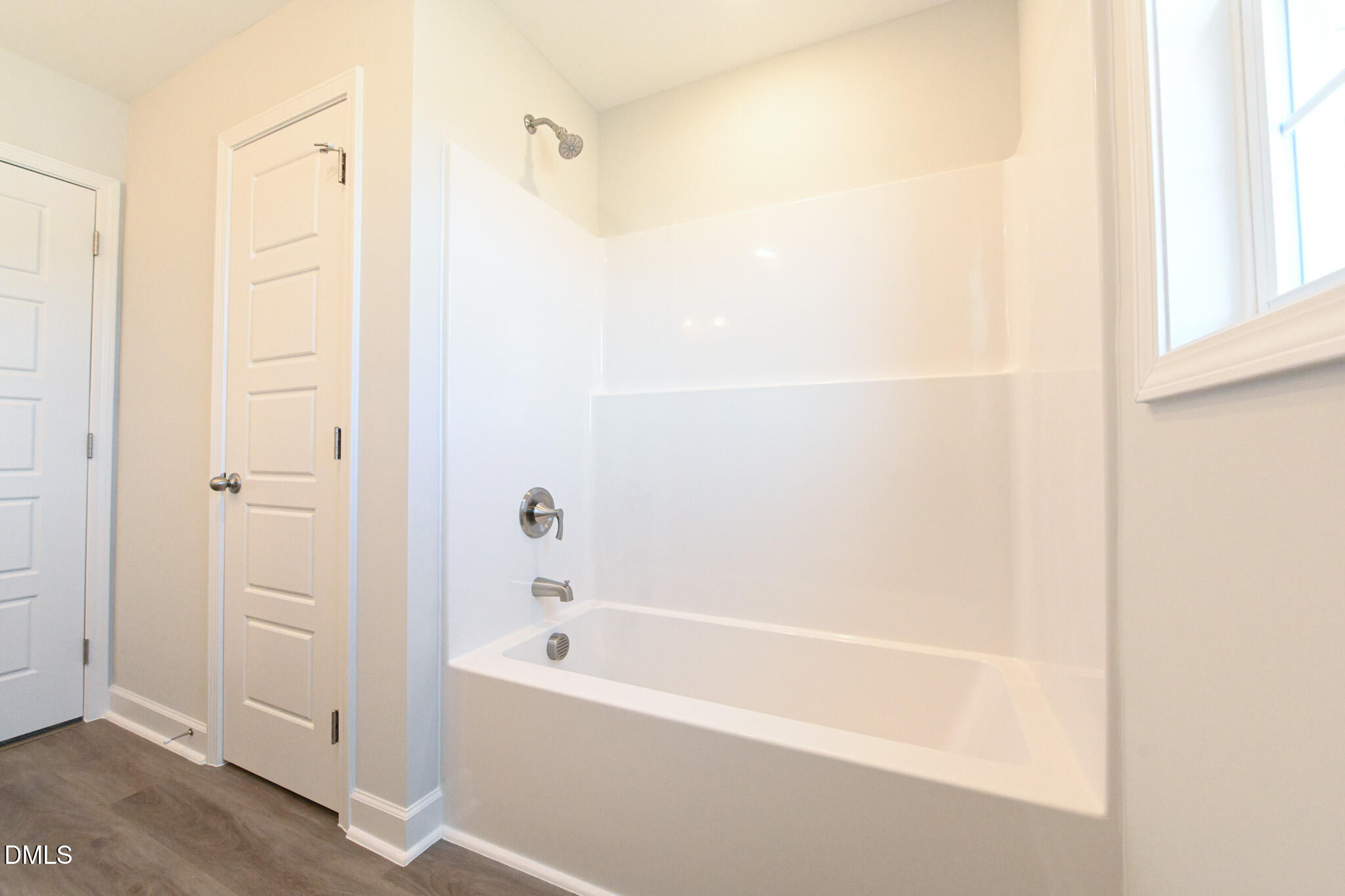Bathroom with a white tub and shower, chrome fixtures, and a sunlit window.
