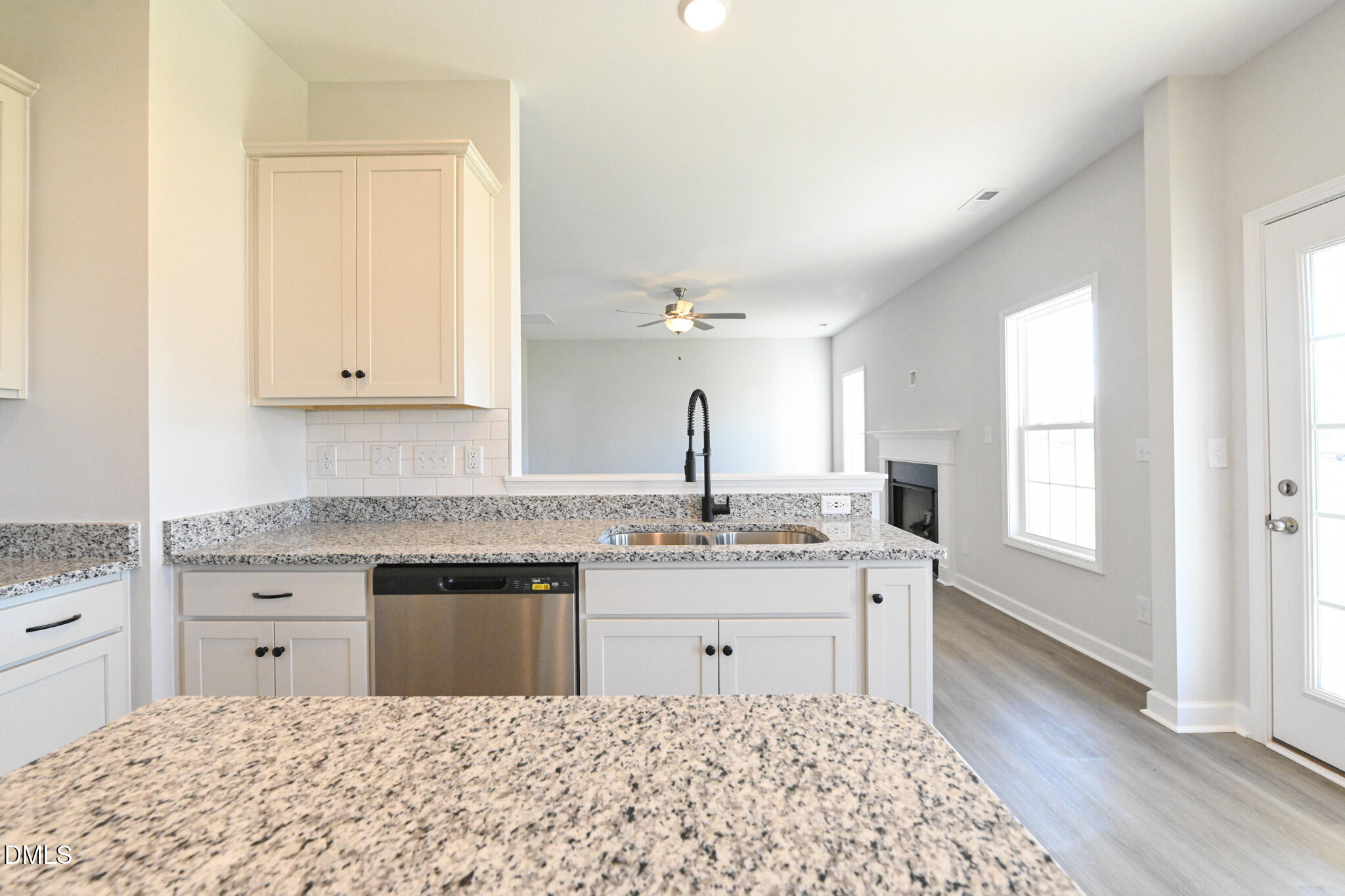 Kitchen with granite counters, white cabinets, double sink, and an open view into the living area.