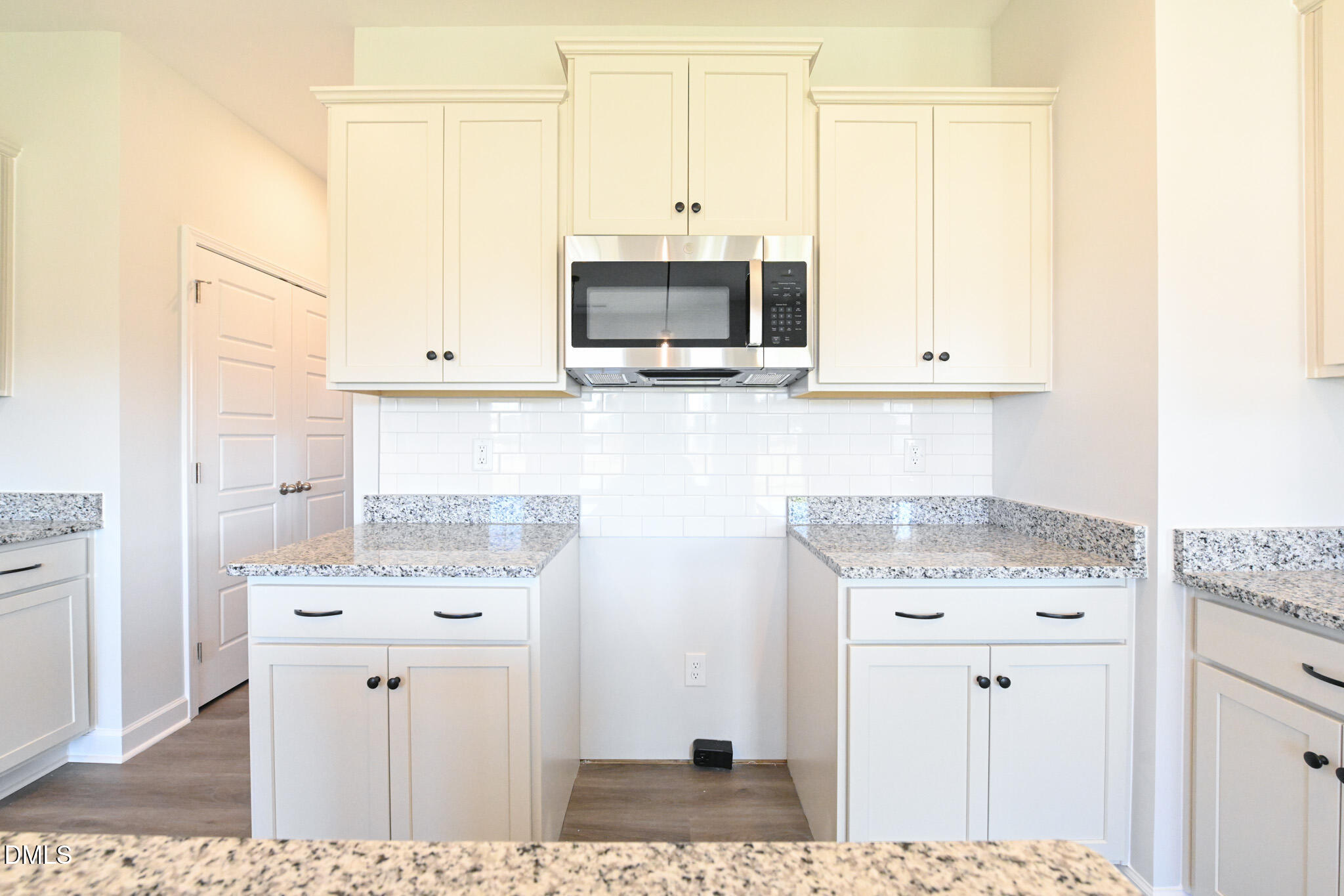 Kitchen with white shaker cabinets, stainless steel microwave, subway tile backsplash, and granite counters.