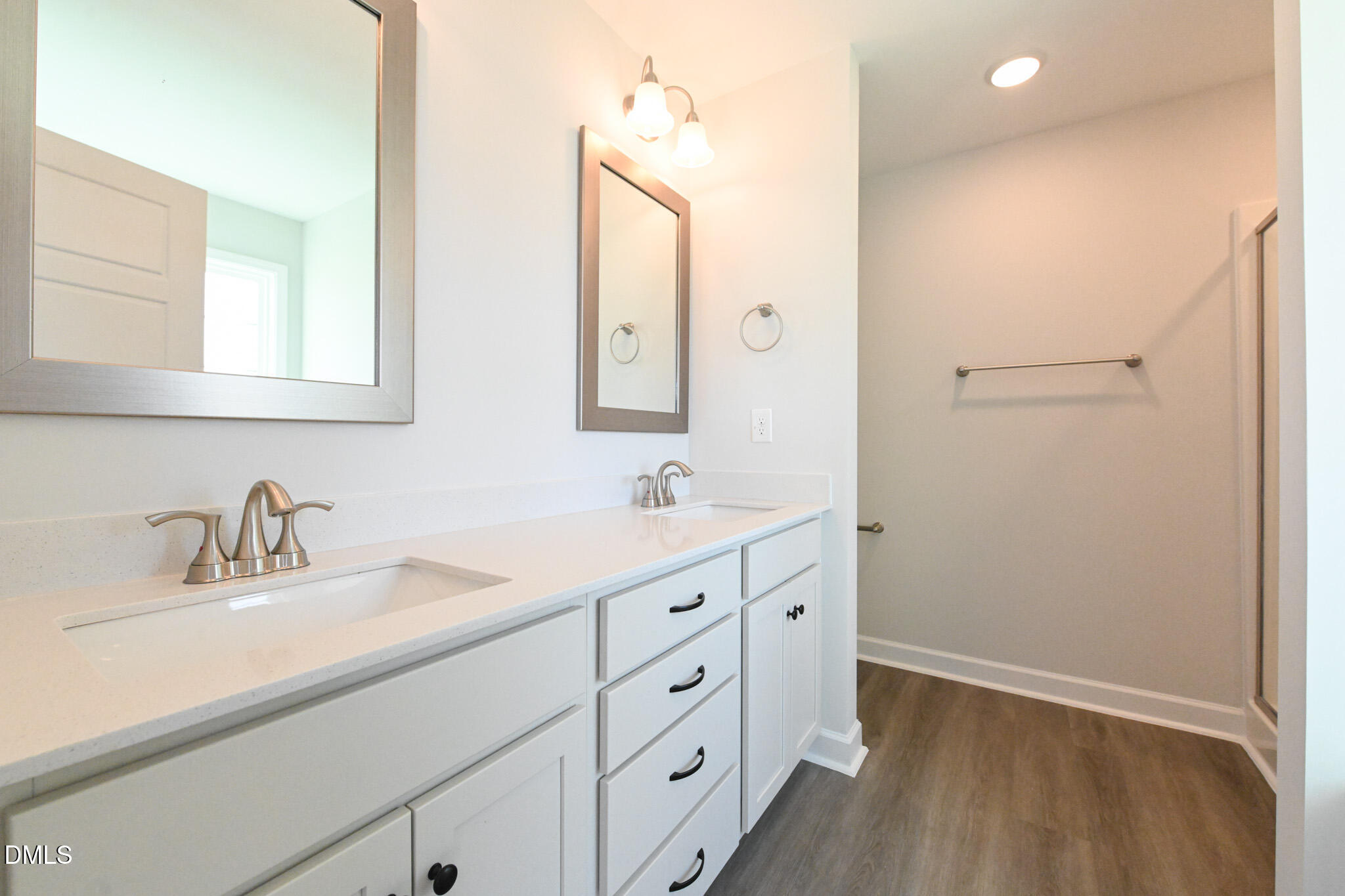 Bathroom with a long white double vanity, framed mirrors, and a spacious walk-in shower area.