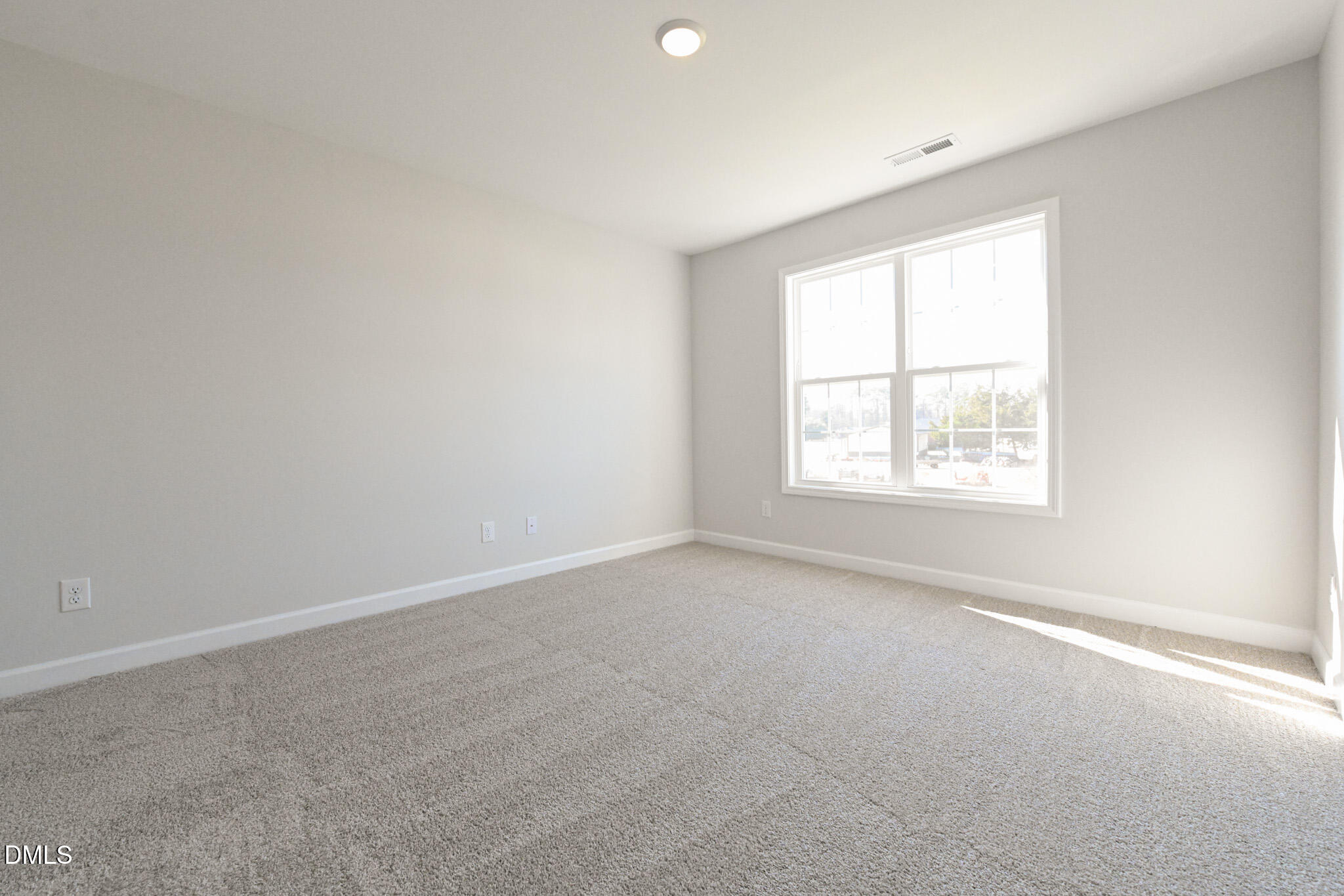 Empty bedroom with beige carpet and a large sunlit double window.