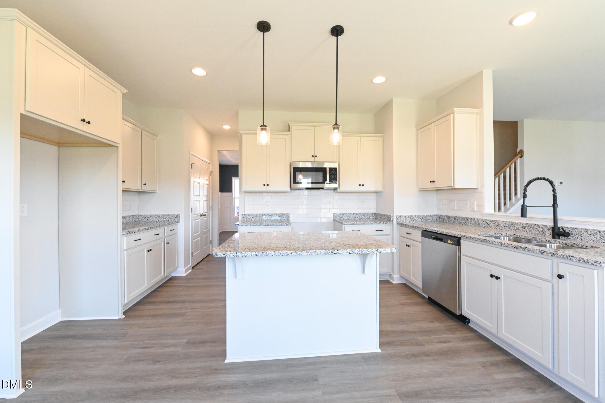 Vacant kitchen with a large granite island, white cabinets, and stainless steel appliances.