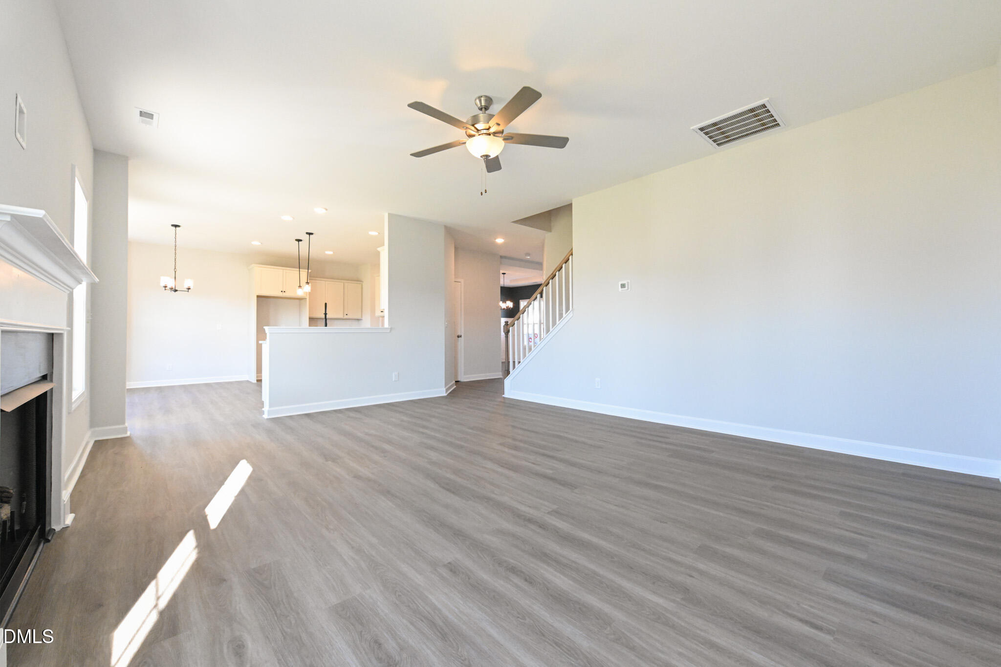 Vacant living room with gray flooring, a fireplace, ceiling fan, and open kitchen and staircase.