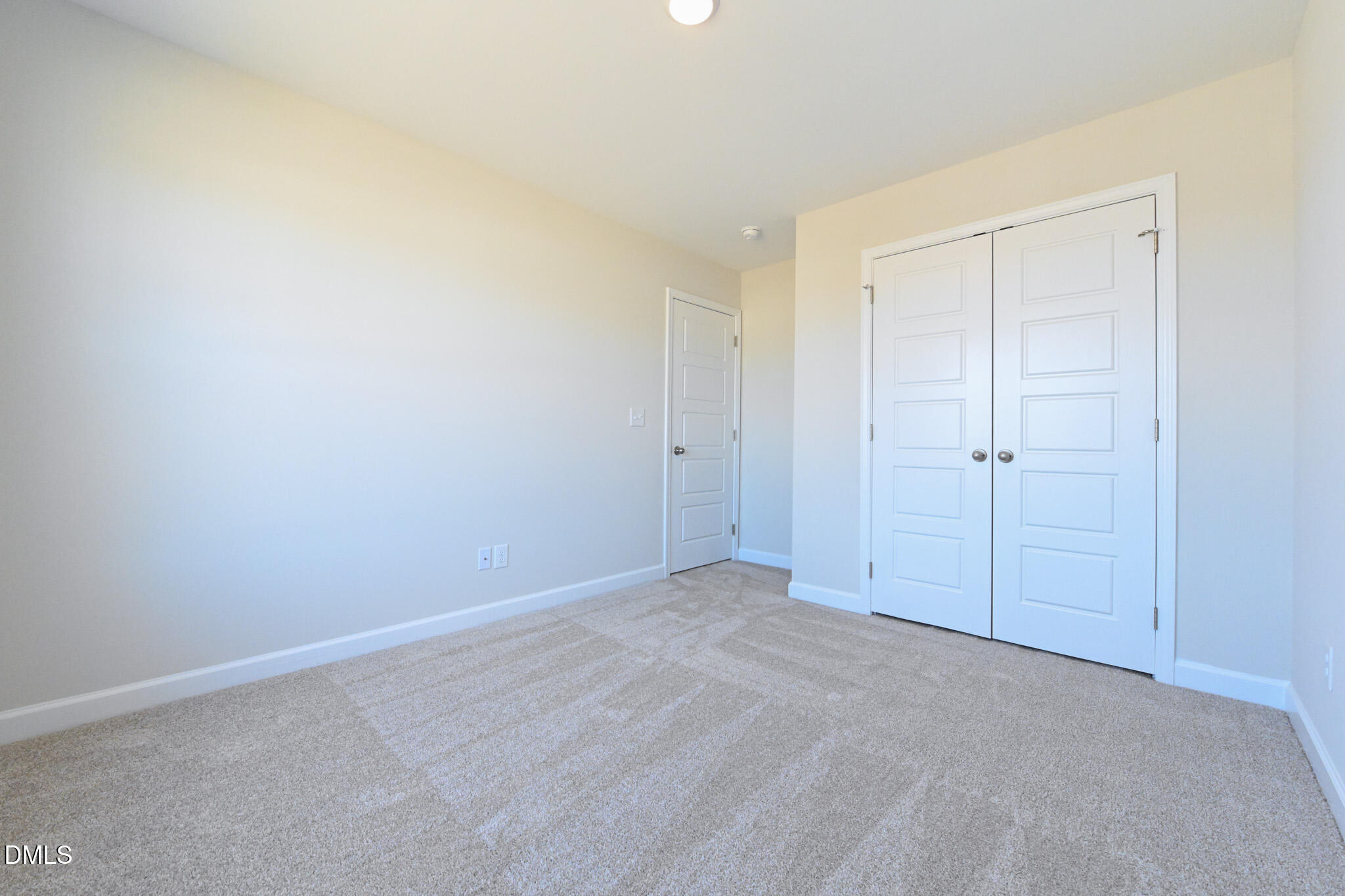 Empty bedroom with beige carpet and white double closet doors.