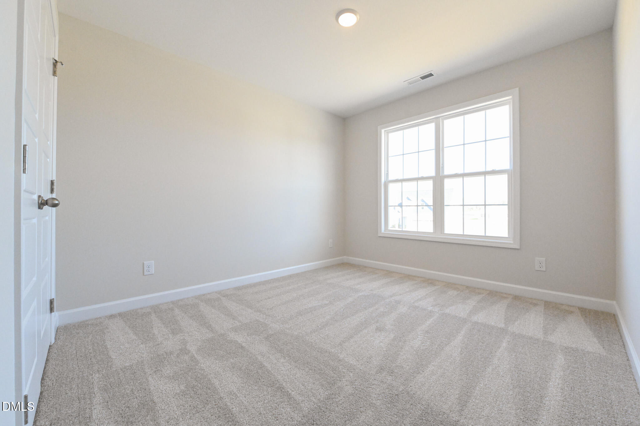 Empty carpeted bedroom with neutral walls and a large gridded window.