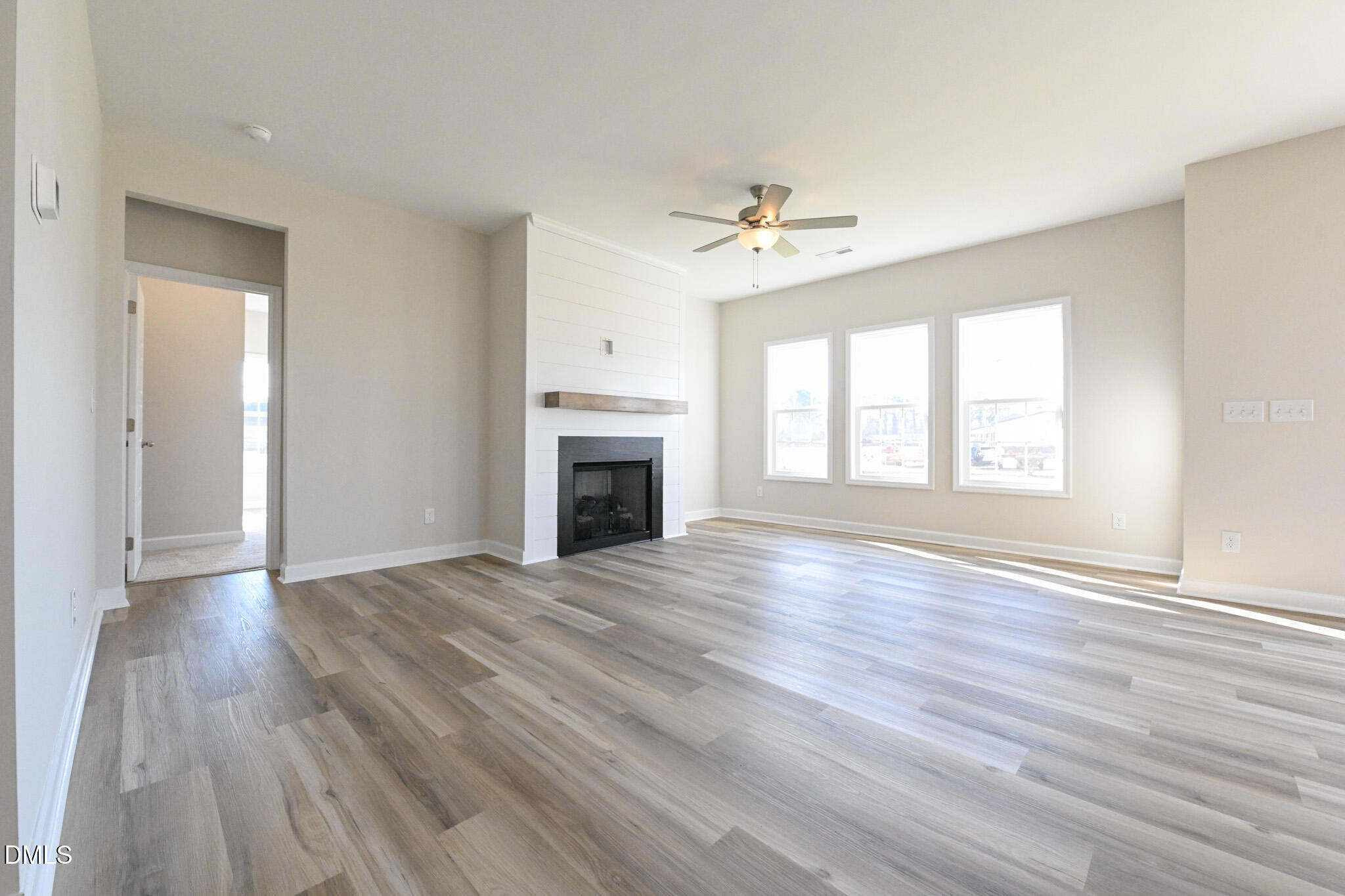 Vacant living room with a shiplap fireplace, gray wood-look floors, and three tall windows.
