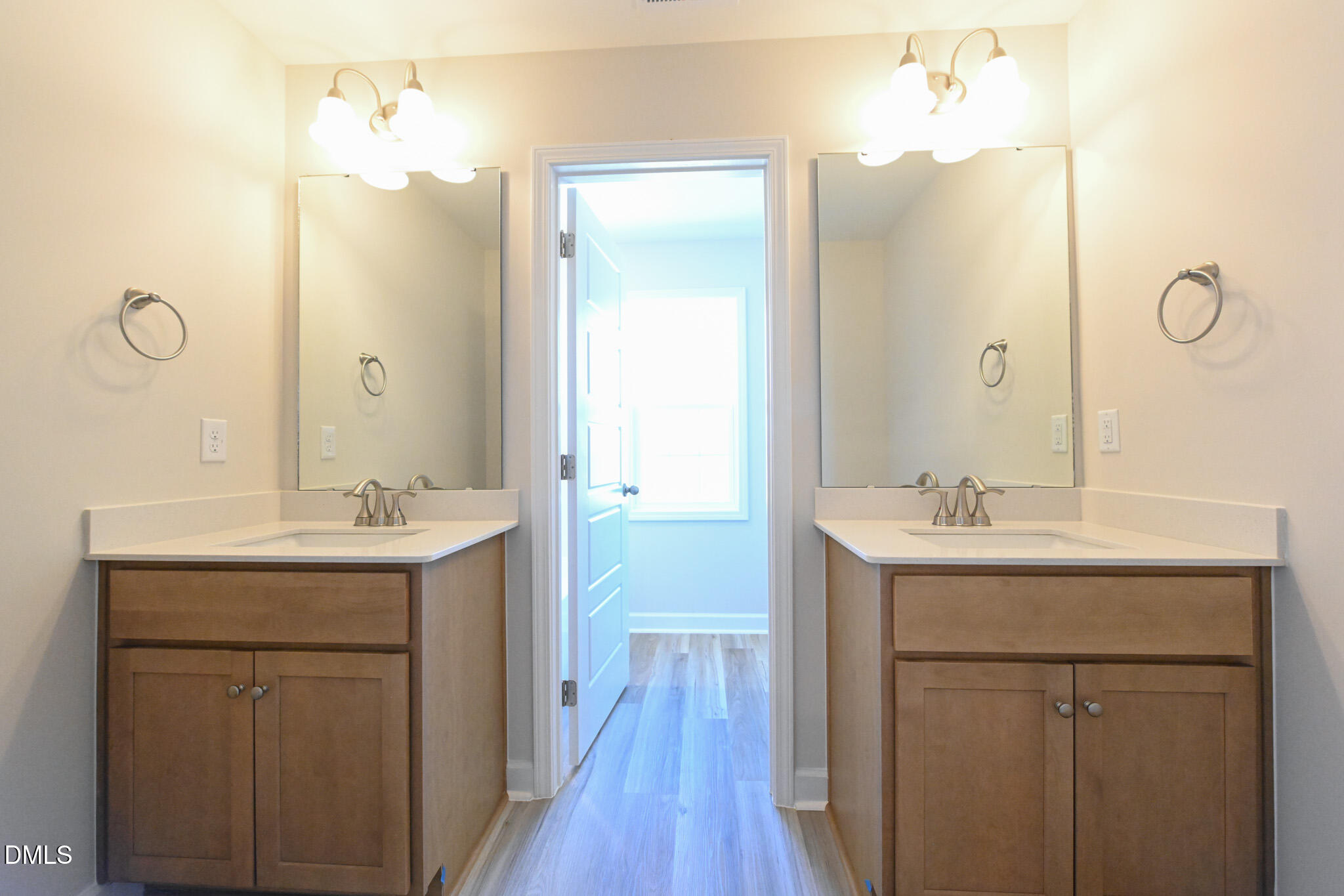 Bathroom with two wood vanities, white countertops, large mirrors, and an open doorway.