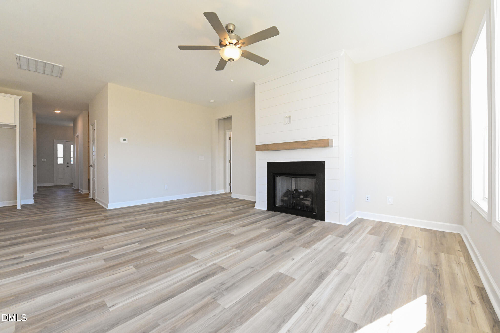 Empty living room with a shiplap fireplace, wood mantel, plank flooring, and ceiling fan.