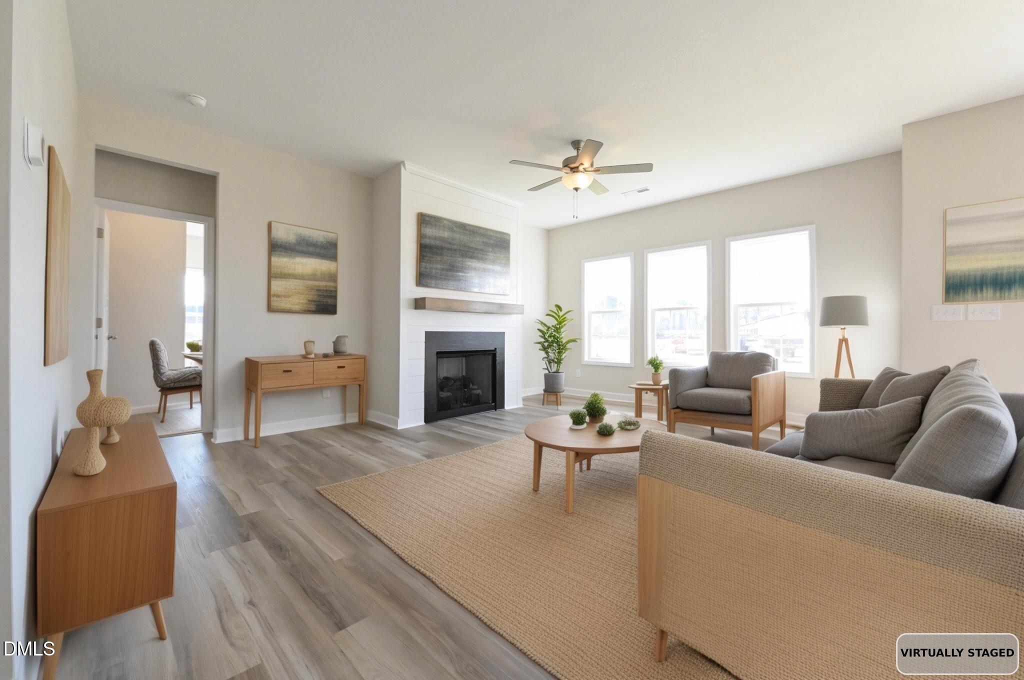Virtually staged living room with a white fireplace, gray sofas, and three large windows.