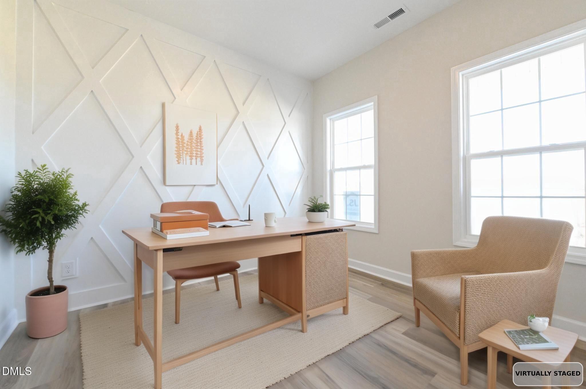 Virtually staged home office with a light wood desk, beige chair, geometric accent wall, and large windows.