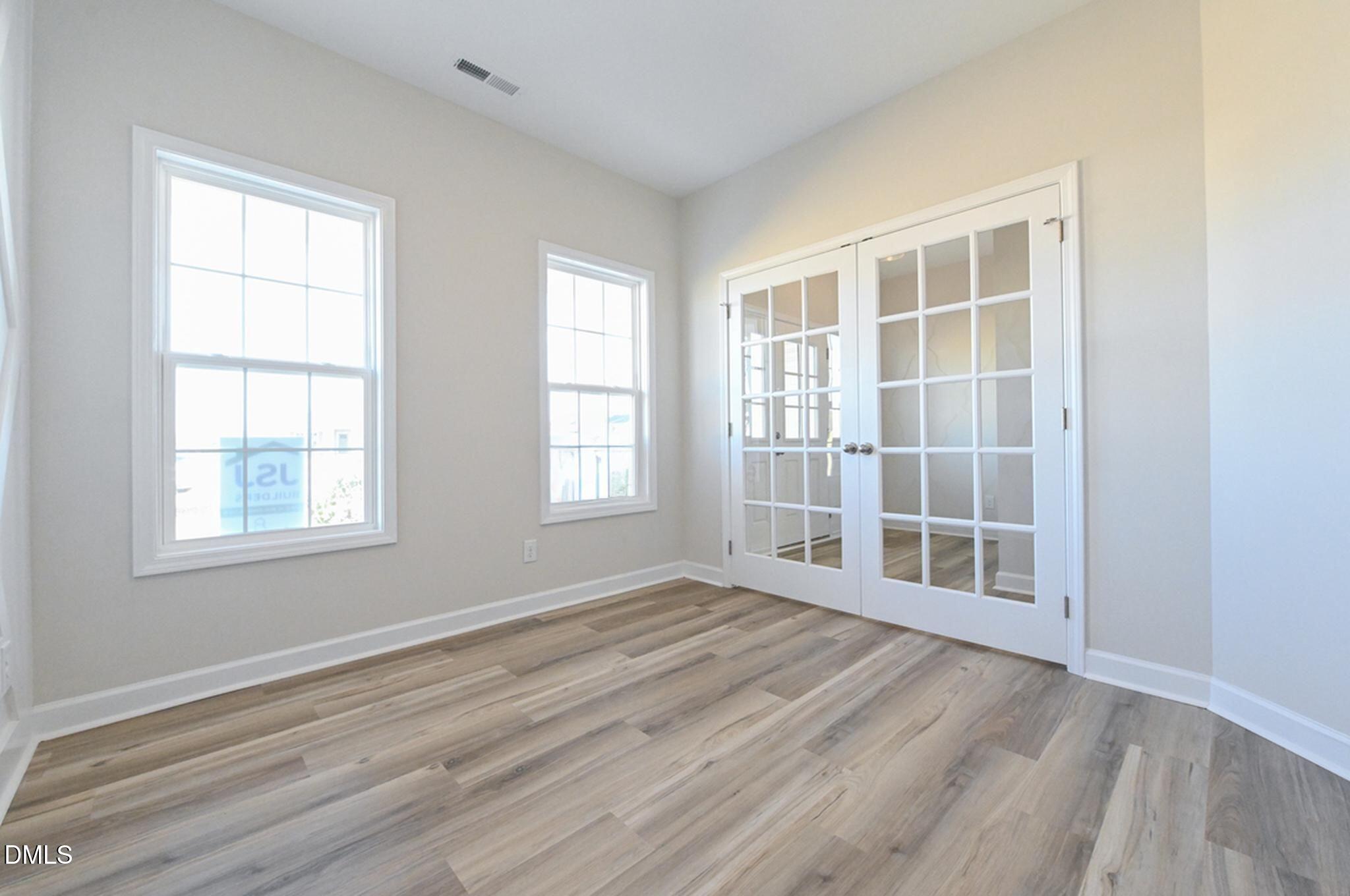 Empty room with wood-look flooring, two windows, and glass-paneled double doors.