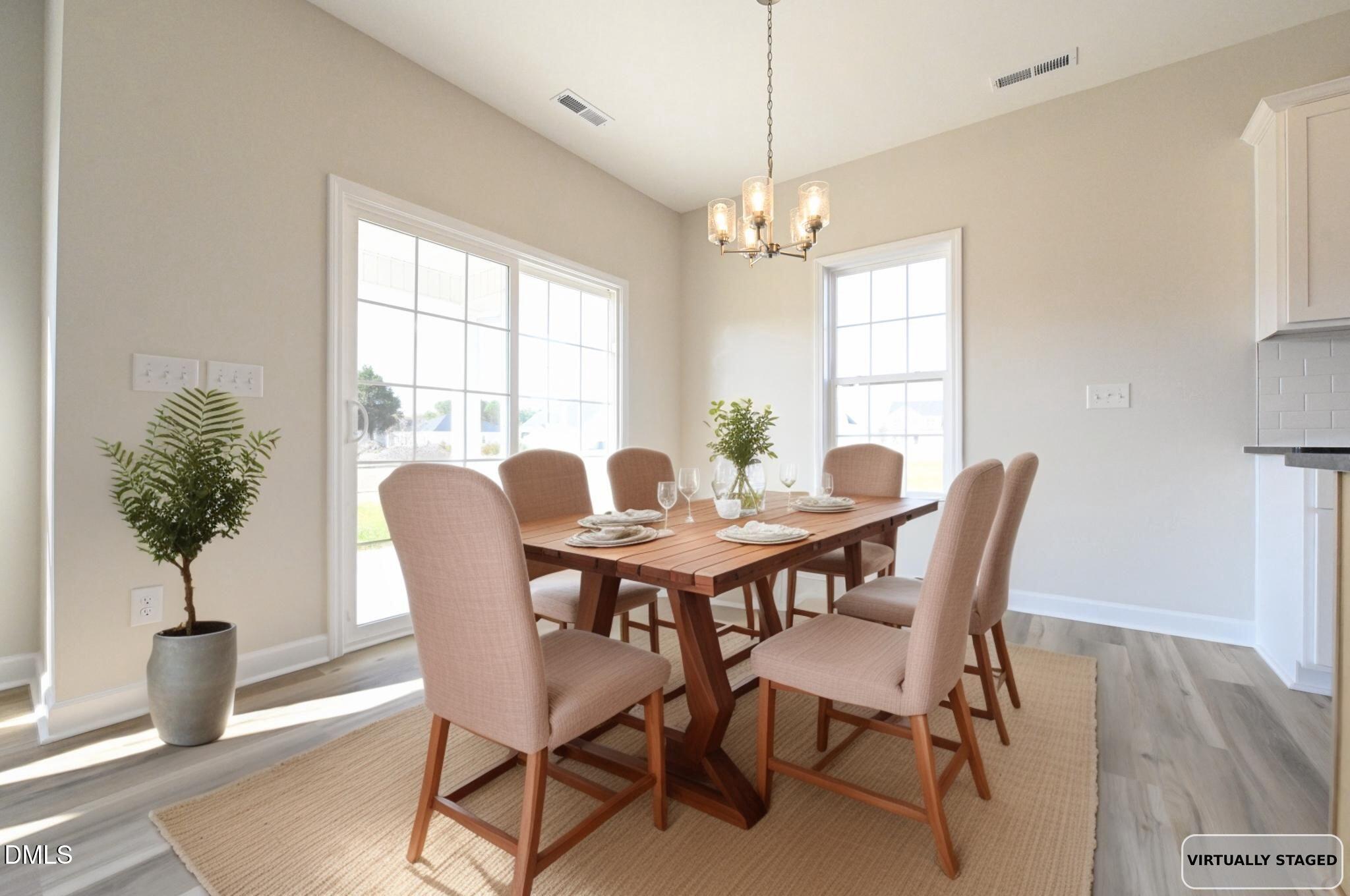 Dining room with a set wooden table, upholstered chairs, chandelier, and large windows.