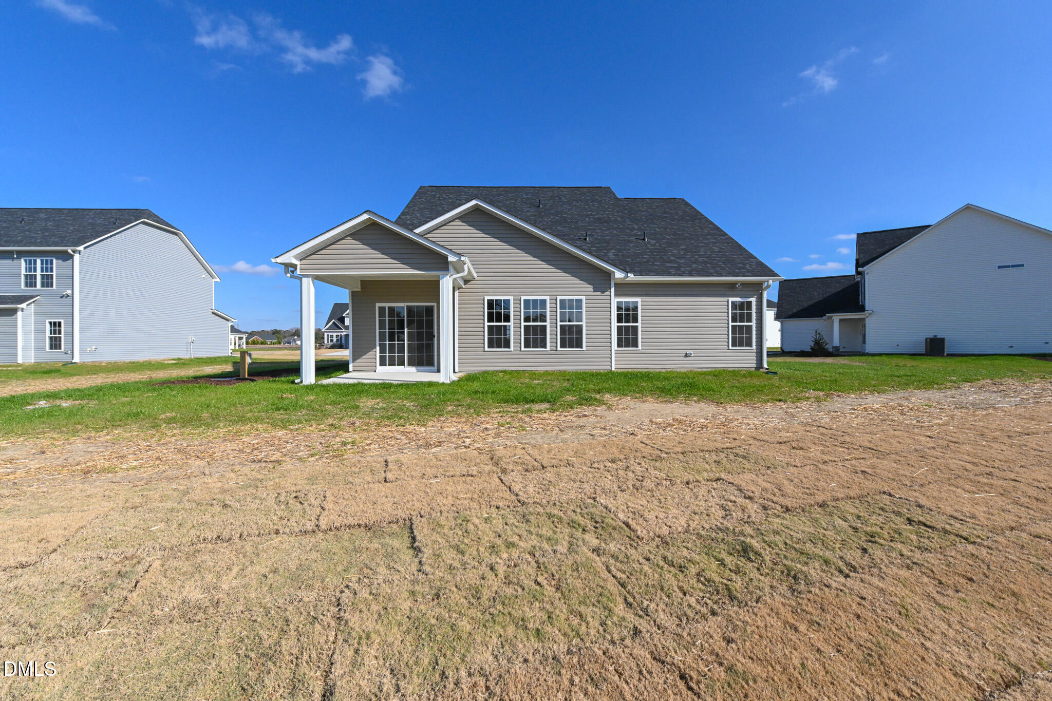Rear of a beige-sided house with a covered patio and broad lawn.