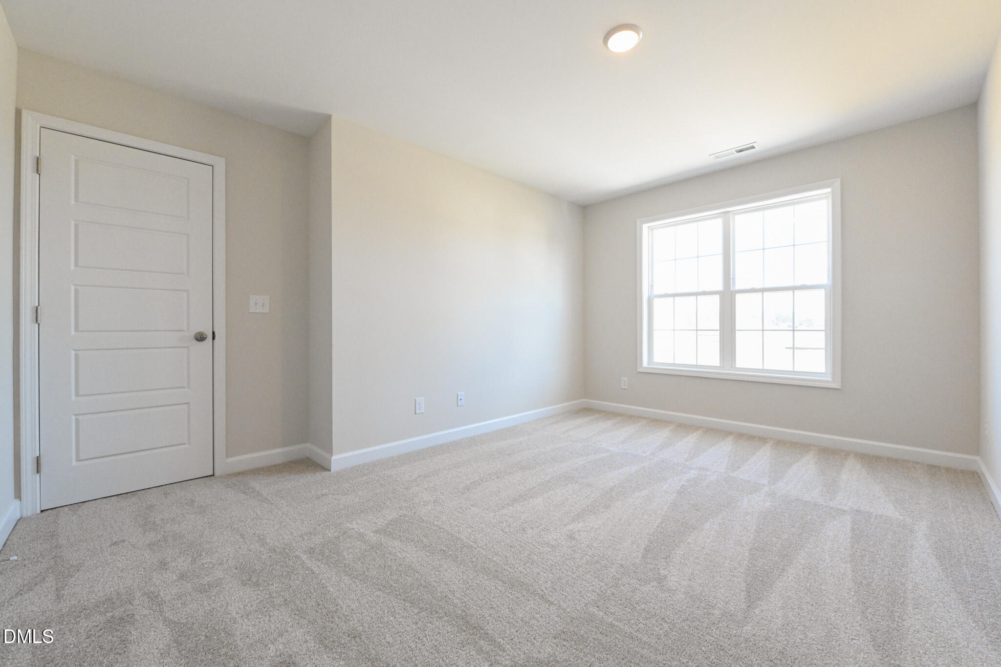 Empty carpeted room with a white paneled door and large multipane window.