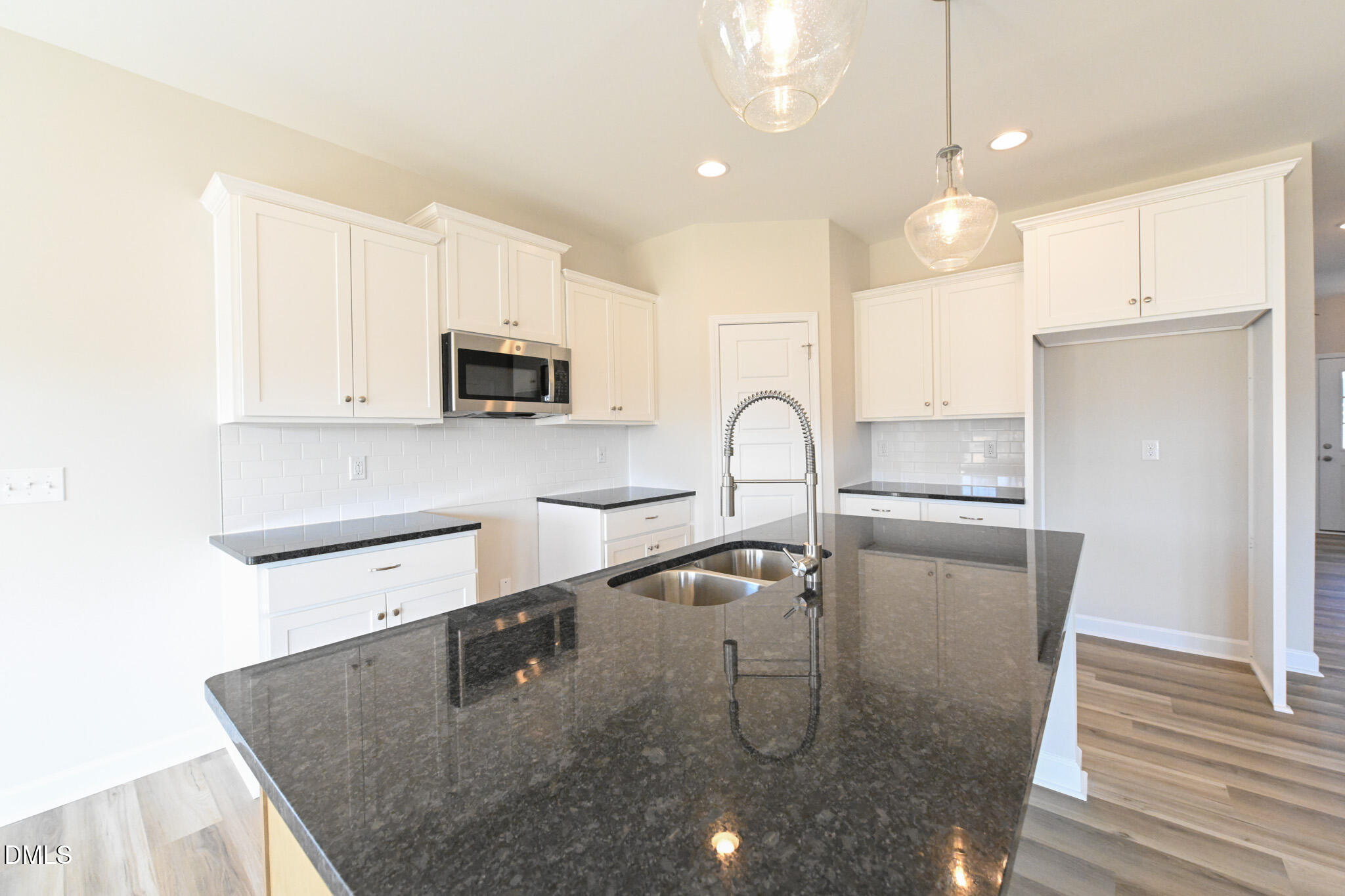 Unfurnished kitchen with white cabinets, dark stone island, double sink, and stainless steel microwave.