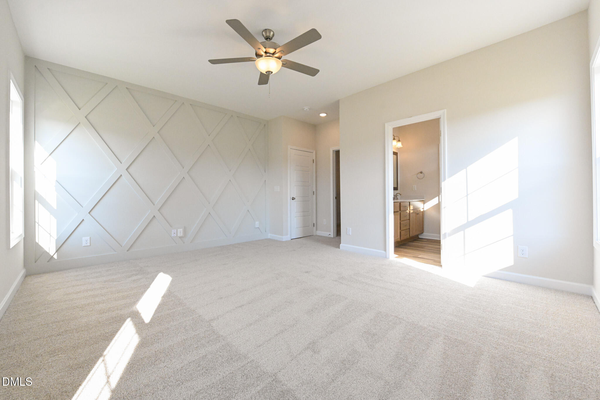 Vacant bedroom with a geometric accent wall, beige carpet, and an adjoining bathroom.